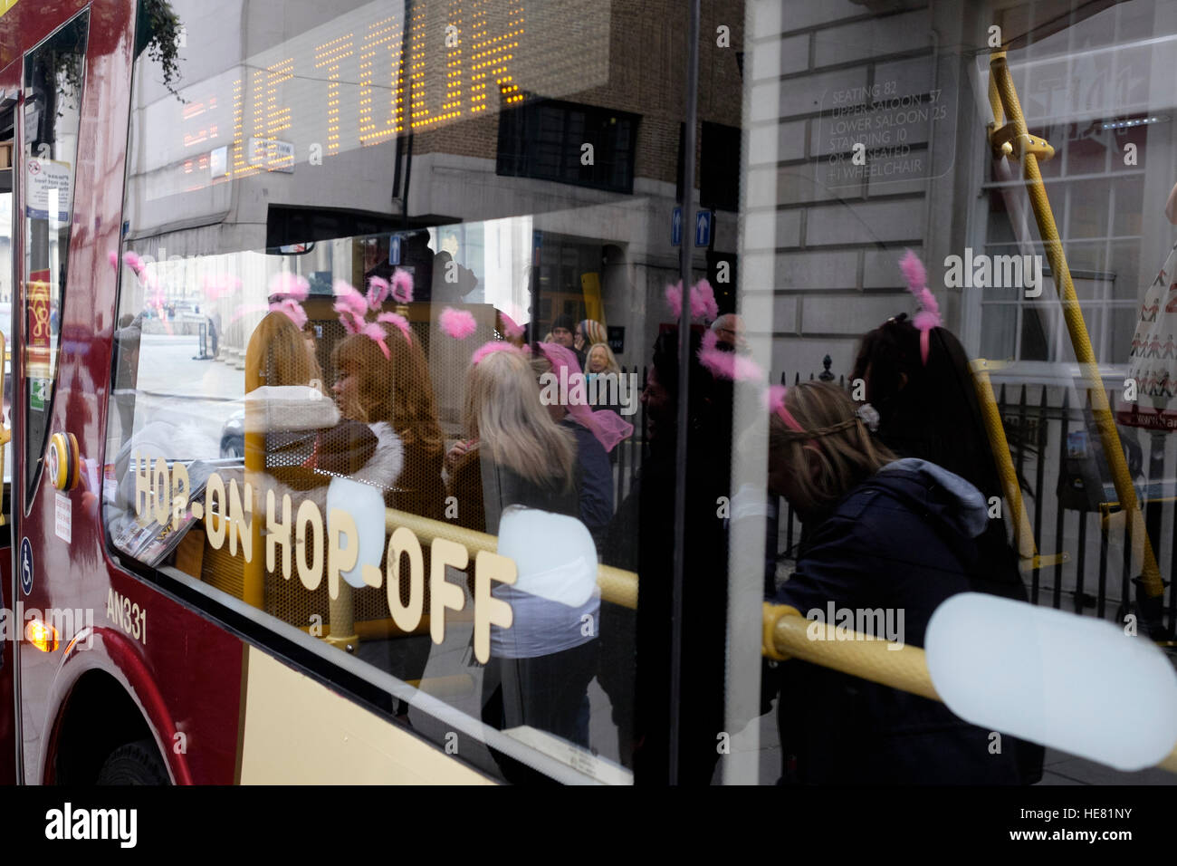 La riflessione su un hop on hop off finestra buss di donne che indossano bunny orecchie mentre su una gallina fare a Londra Foto Stock