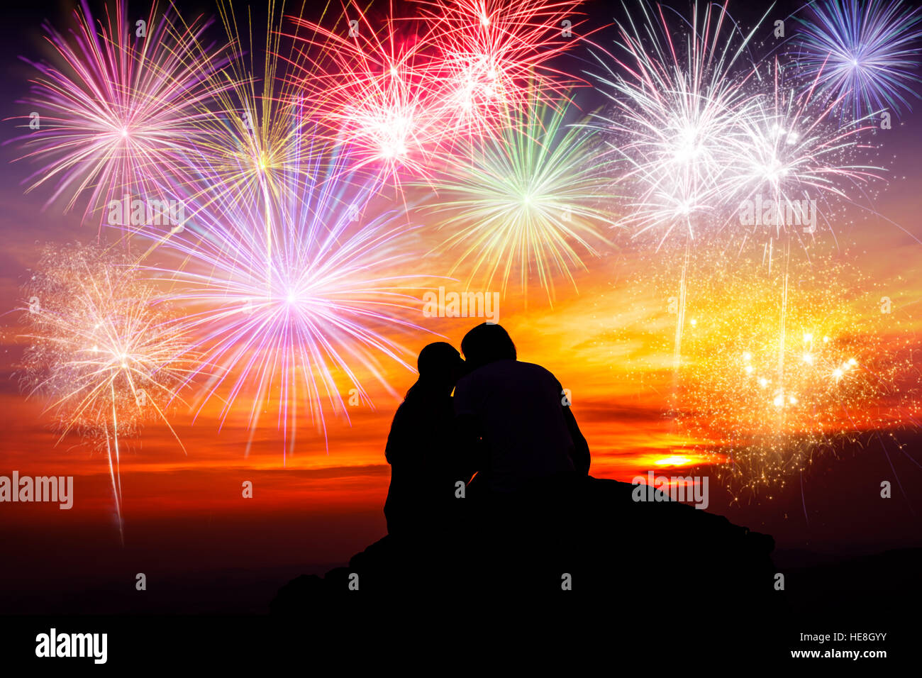Felice coppia seduta sul pavimento, kissing ogni altra e guardare i fuochi d'artificio colorati Foto Stock
