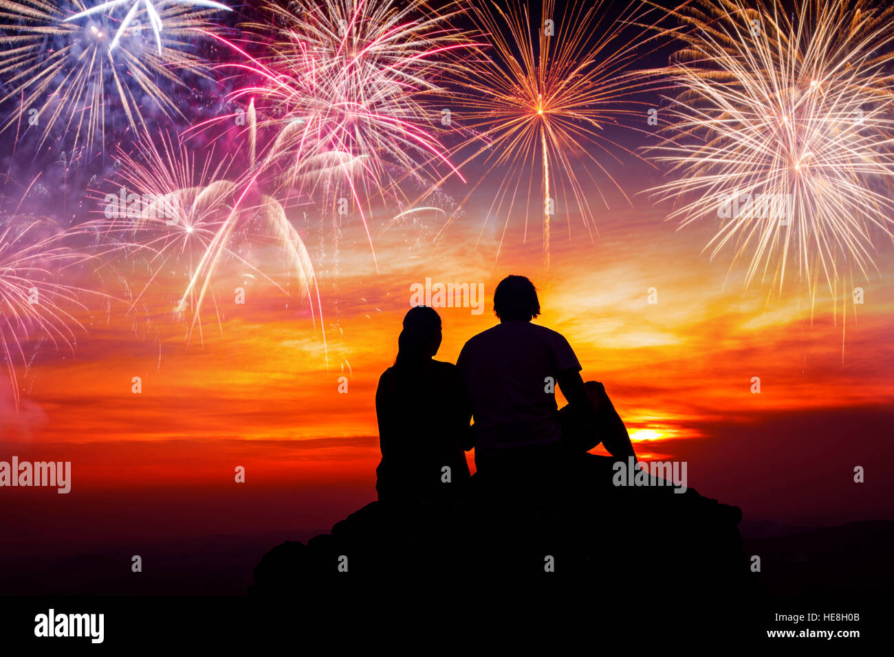 Felice coppia seduta sul pavimento e guardare i fuochi d'artificio colorati Foto Stock