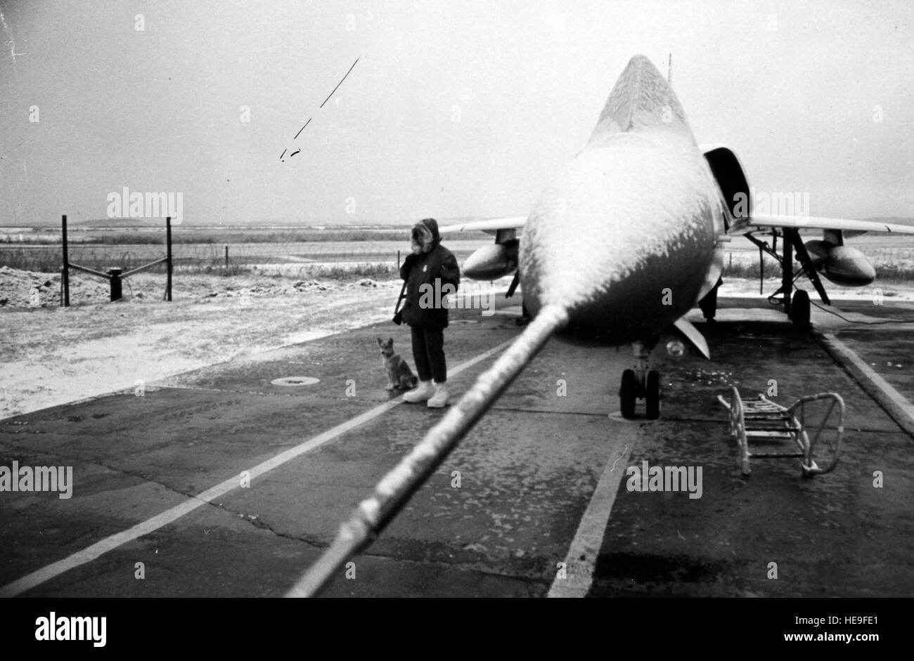 Un aereo F-106A siede sulla neve presso la base aerea di Osan, Corea del Sud, mentre una guardia di polizia di sicurezza supervisiona un addestratore di cani da guardia, dimostrando le operazioni di base invernali e le misure di protezione degli aeromobili. Foto Stock
