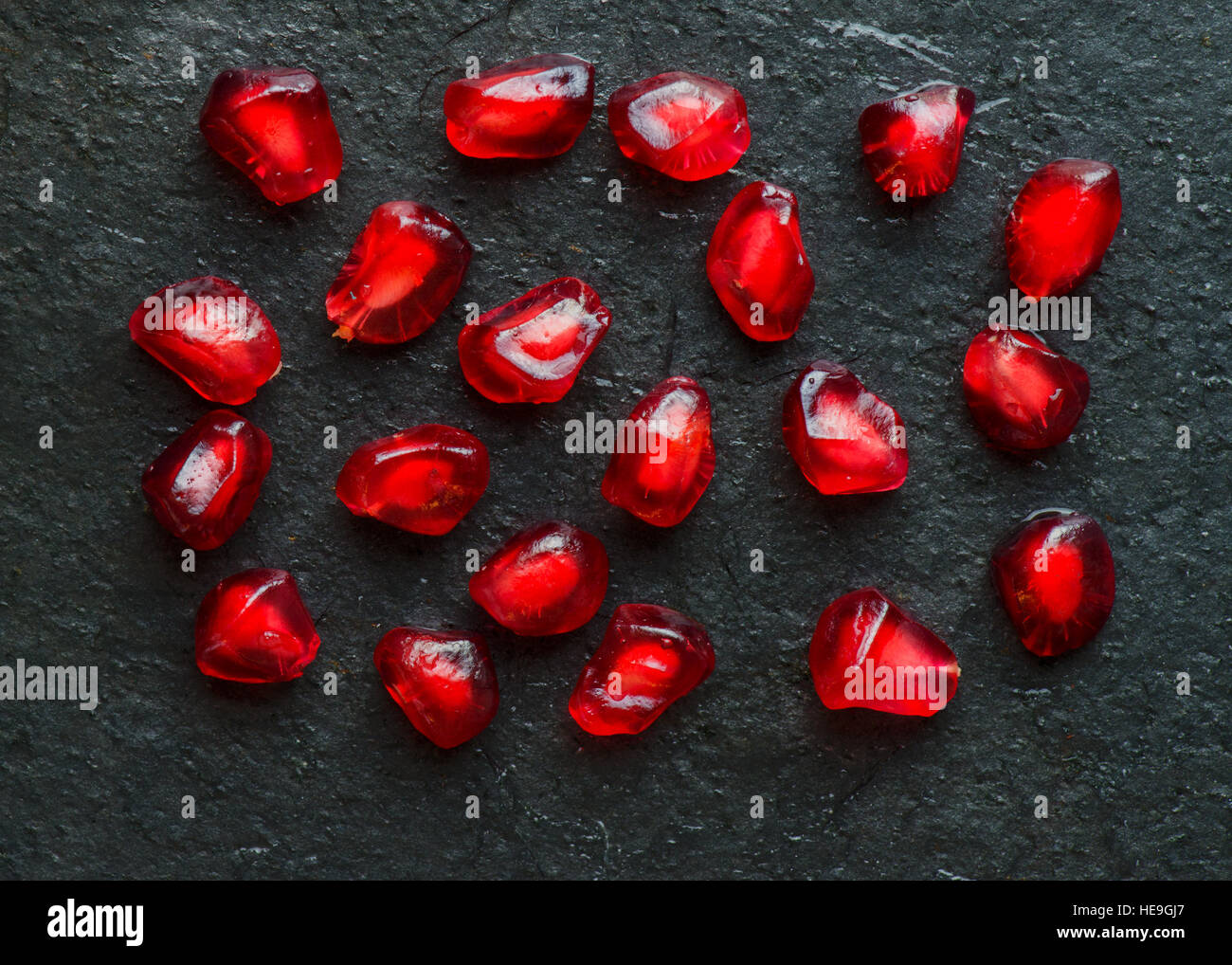 Ricca immagine astratta di un gruppo di singoli red melagrane semi sulla pietra nera ardesia Foto Stock