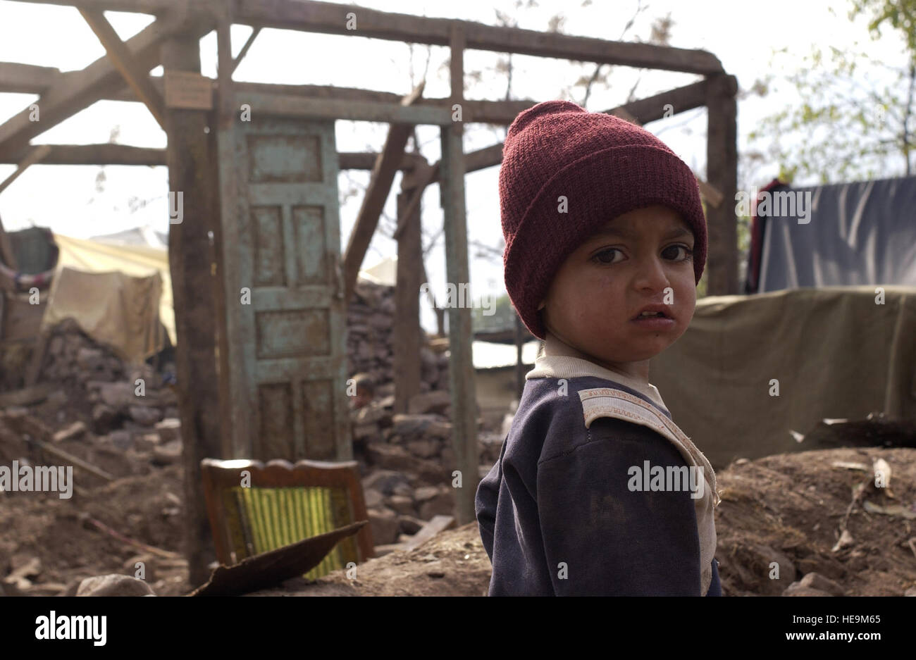 Un bambino passeggiate attraverso le macerie di una casa distrutta che viene ricostruito dagli sforzi combinati degli abitanti dei villaggi, i militari pakistani e marinai DEGLI STATI UNITI a Miani Bandi vicino a Muzaffarabad, Pakistan, Dicembre 3, 2005. Stati Uniti Navy Seabees assegnato alla Naval Mobile Battaglione di costruzione 74 sono strutture edili per sfollati terremotati a Miani bandi. L'esercito degli Stati Uniti sta partecipando in assistenza umanitaria alle operazioni a sostegno di Il pakistan-led gli sforzi di rilievo per portare aiuto alle vittime del terremoto che ha colpito la regione di Ottobre 8, 2005. Airman 1. Classe Barry Loo) Foto Stock