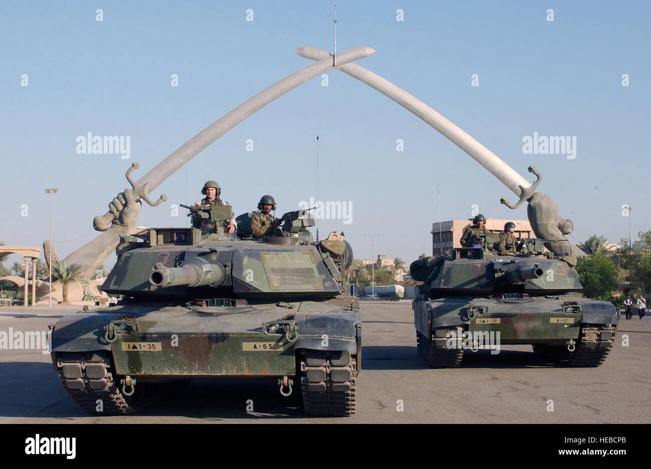 US Army (USA) M1A1 Abrams MBT (battaglia principale serbatoio), e personale da una società (CO), Task Force° Battaglione, 35th Armor Regiment (1-35 Armor), 2° Brigata Combat Team (TDB), 1° Divisione Corazzate (AD), posano per una foto sotto il "Mani di Vittoria" cerimonia in Piazza, Baghdad, Iraq durante l'Operazione Iraqi Freedom. Le mani di vittoria monumento costruito alla fine della guerra Iran-Iraq segna l'entrata di una grande parata a terra nella zona centrale di Baghdad. La mano e il braccio sono modellati dopo che l ex dittatore Saddam Hussein la propria e circondato con migliaia di caschi iraniano preso dal campo di battaglia. Il Foto Stock