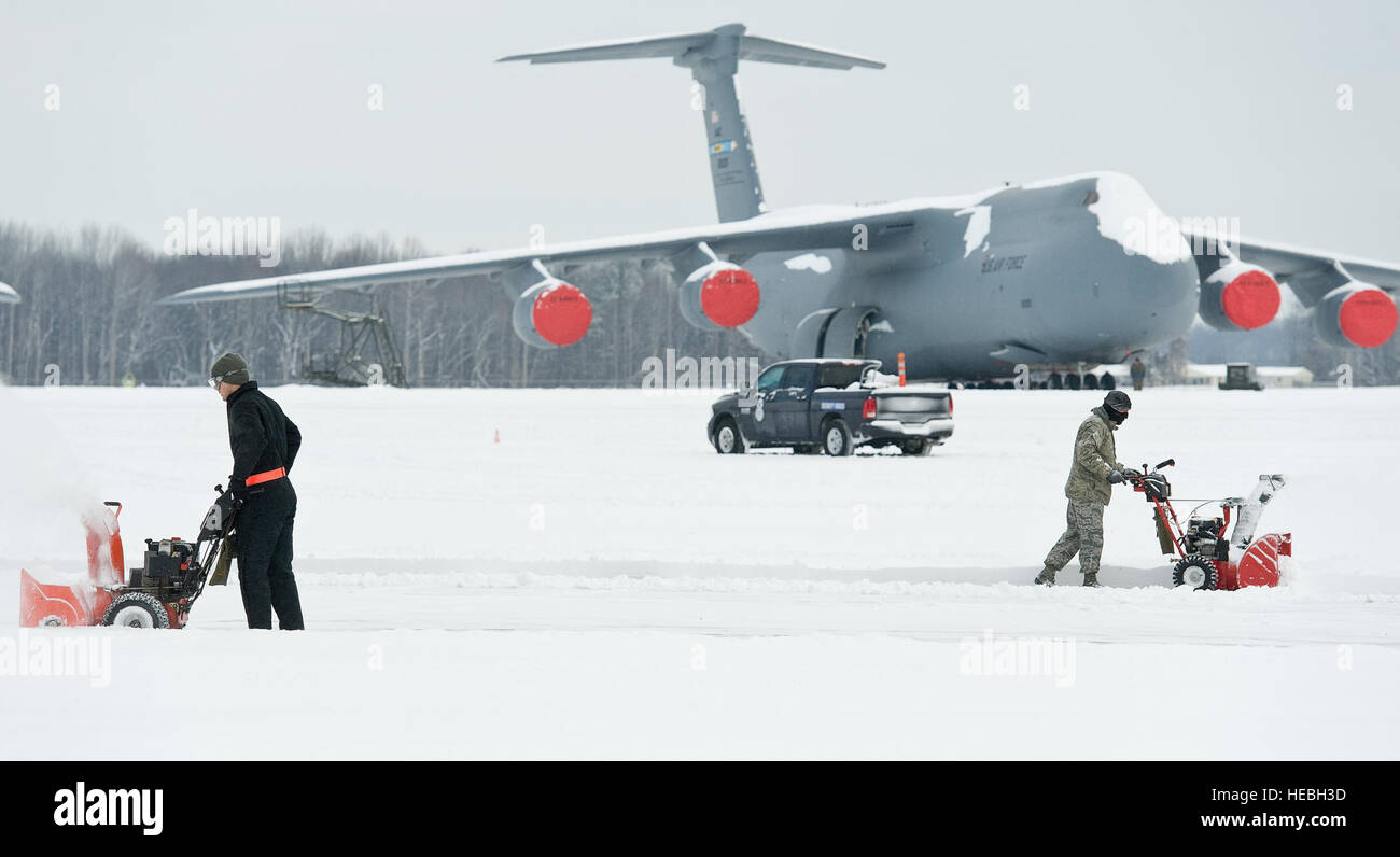 Una C-5M Super Galaxy siede sulla linea di volo come due team membri di dover utilizzare frese per la neve a cancellare la presenza di neve tra due aeromobili hangar di manutenzione Febbraio 17, 2015, a Dover Air Force Base, Del. tempesta invernale Octavia oggetto di pratiche di dumping per un totale di 4 pollici di neve sulla base e area locale ala richiesta di conferma la leadership di avviare due ore di ritardo di reporting per la missione essenziale di livello 2 e 3 personale. (U.S. Air Force foto/Roland Balik) Foto Stock