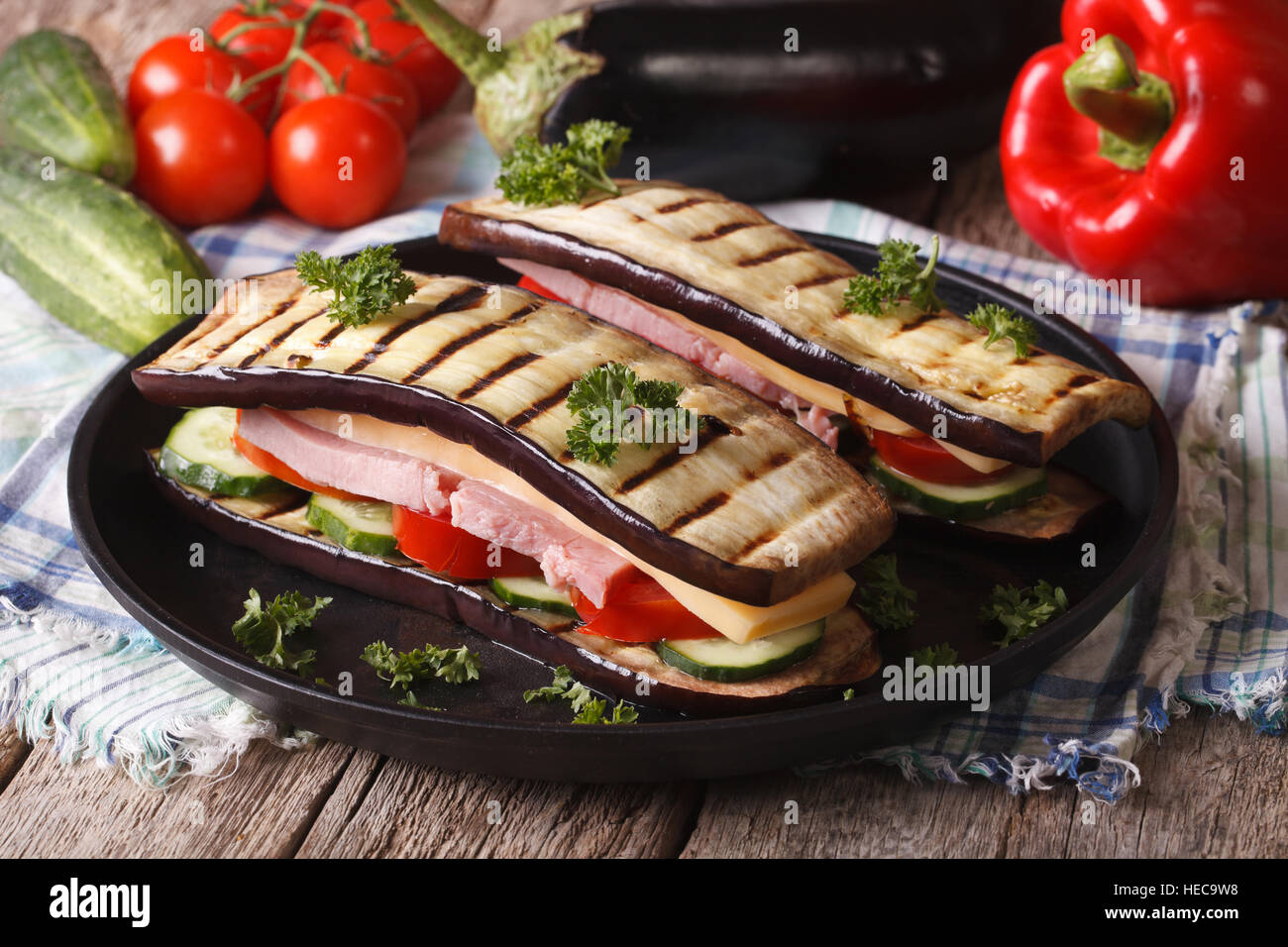 Creative sandwich di melanzane con verdure fresche, prosciutto e formaggio close-up su una piastra. Foto Stock