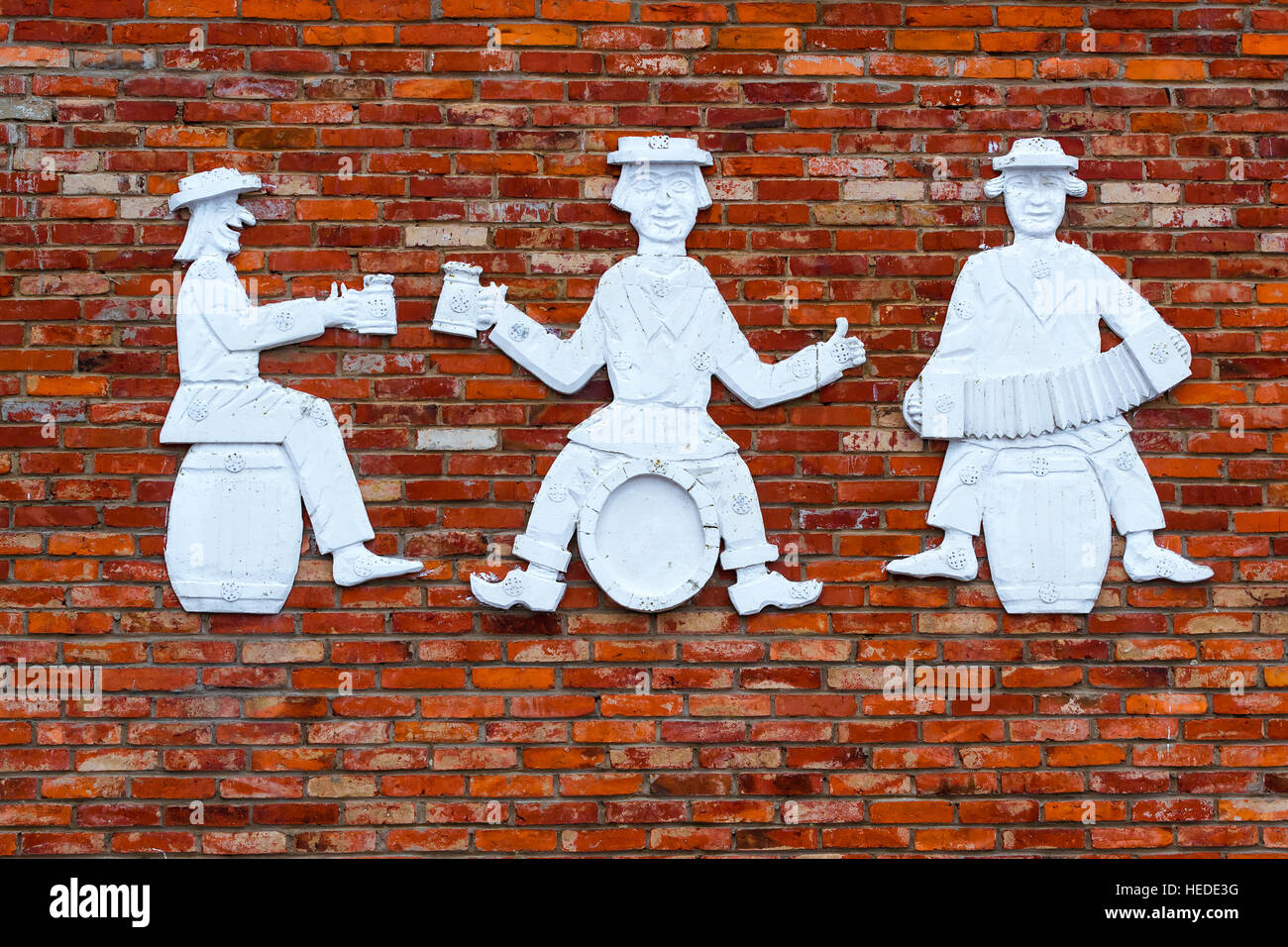 Figure in pietra di tre uomini su un muro di mattoni. Divertente persone sono seduti su di barili, bere birra e giocare a armonica. Il lituano countrysi provinciale Foto Stock