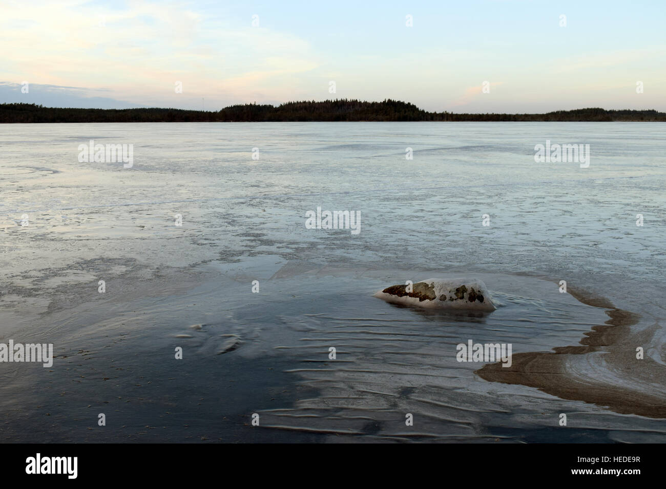 Lago ghiacciato a dicembre. Singola pietra sul primo piano. Foto Stock