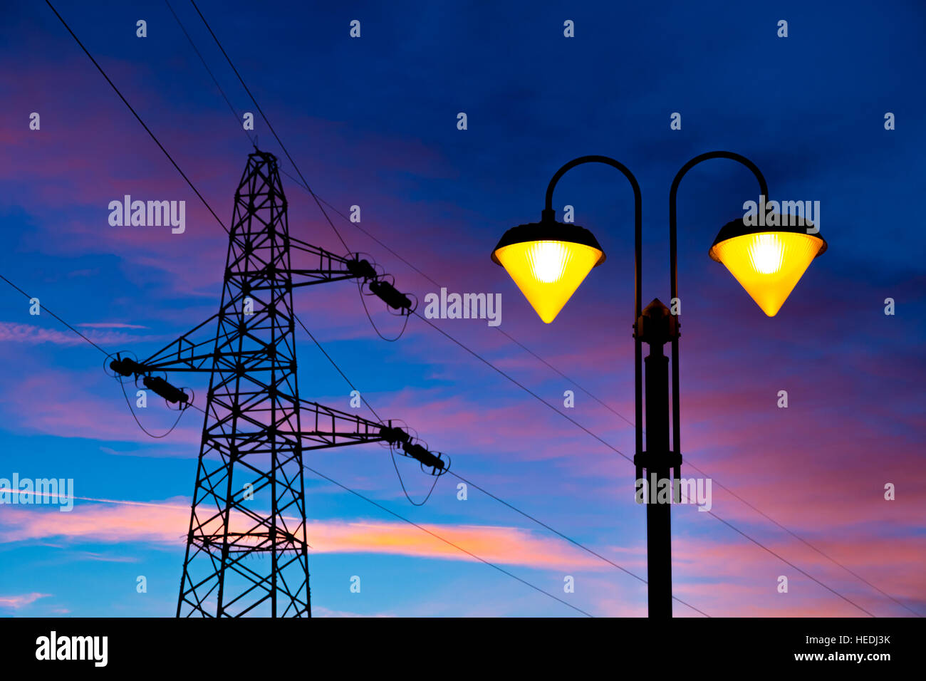 Accesa sul lampione al tramonto con linea ad alta tensione e il pilone sullo sfondo Foto Stock