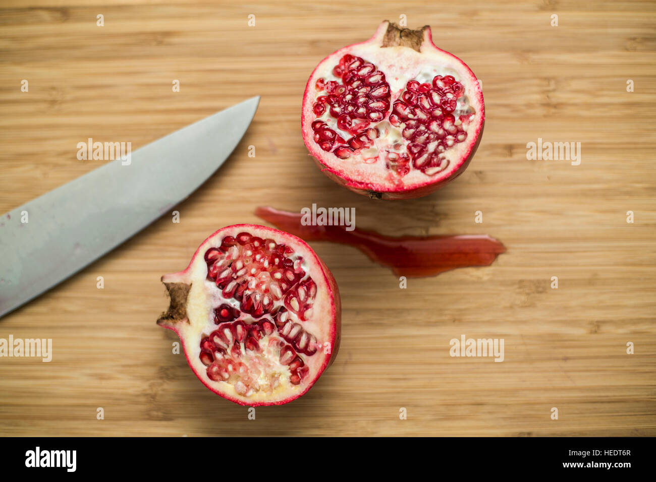 Un grande melograno affettato con un coltello su un tagliere di legno, con semi e succo di frutta Foto Stock
