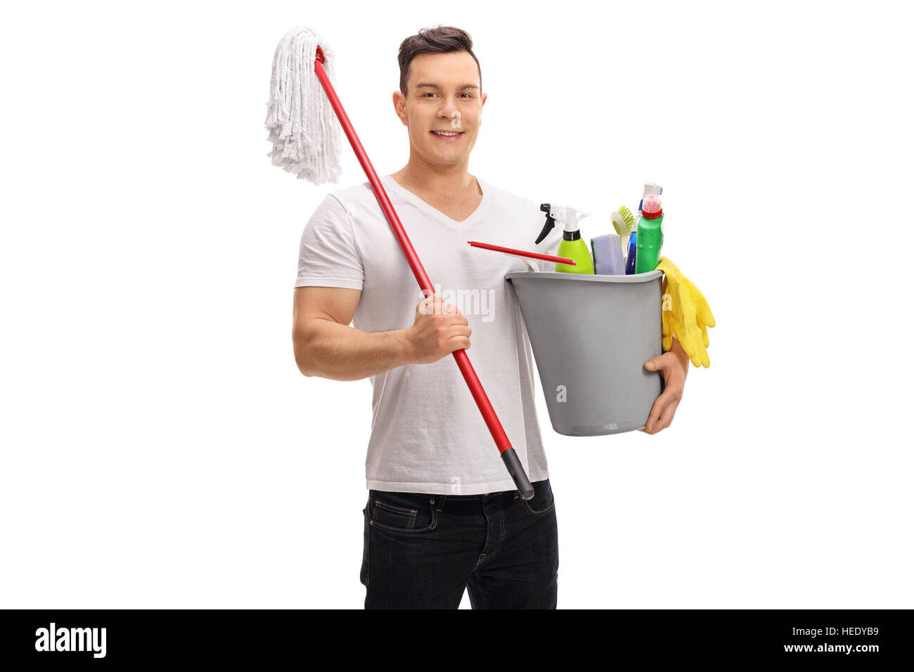 Giovane uomo tenendo un secchio pieno di prodotti per la pulizia e la radazza isolati su sfondo bianco Foto Stock