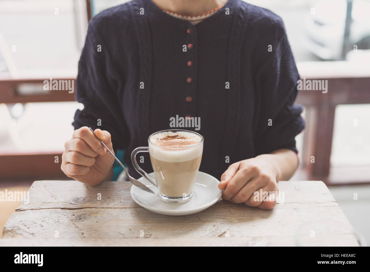 Una giovane donna è seduta al tavolo di un caffè e sta avendo un grande tazza di latte, chai o simili spumeggiante bevanda Foto Stock