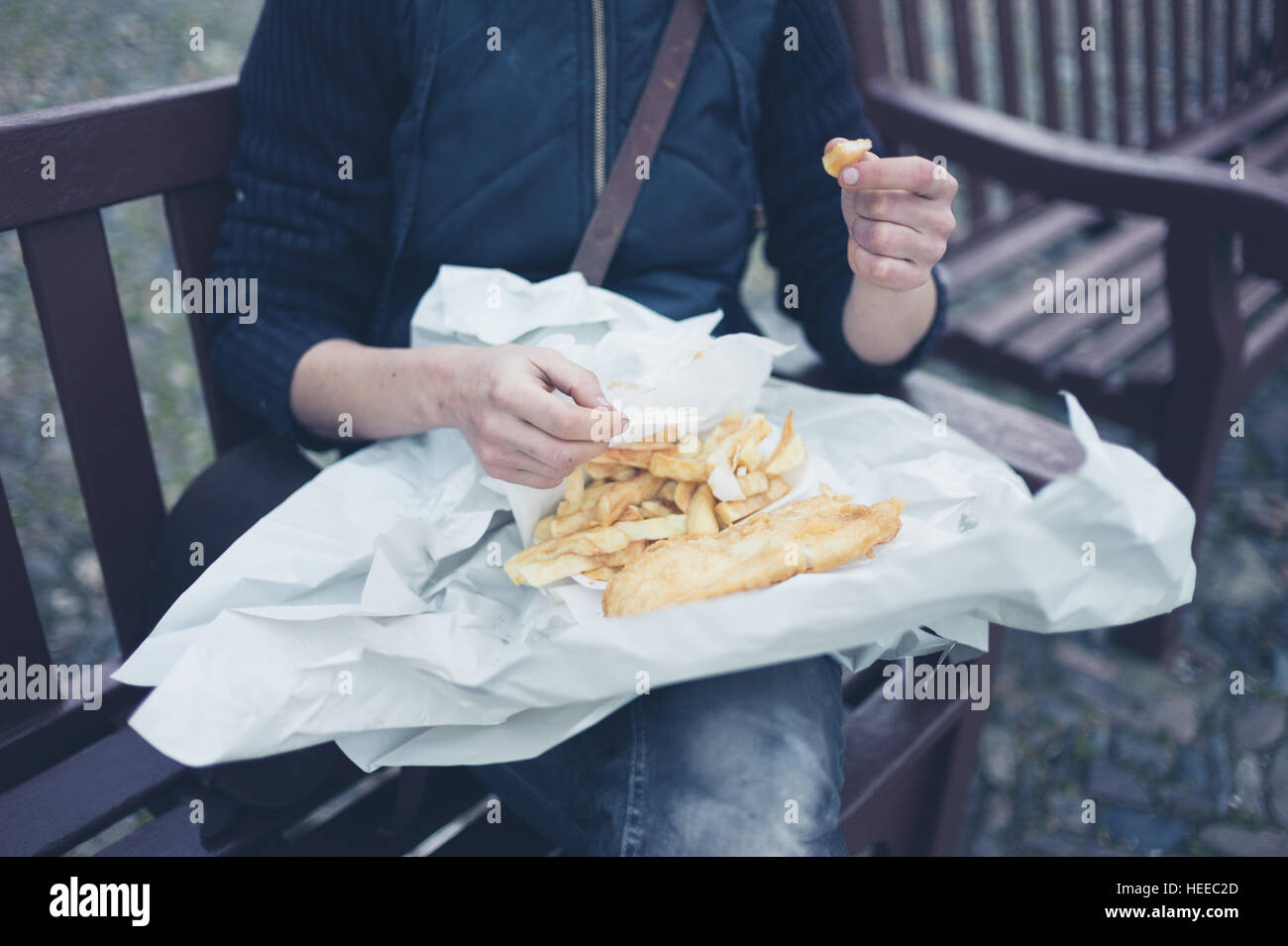 Una giovane donna è seduta al di fuori e sta mangiando pesce e patatine fritte Foto Stock