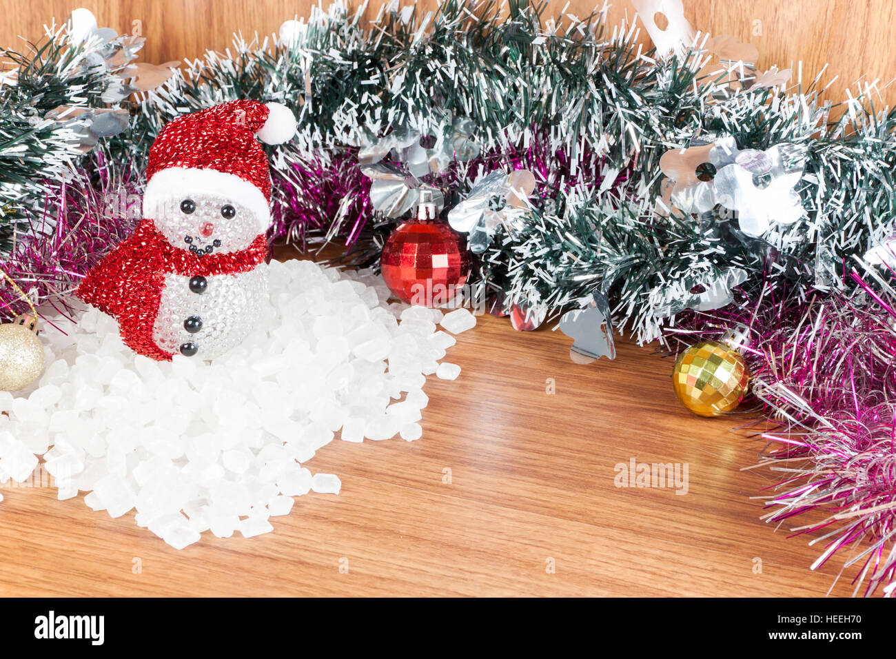 Uomo di neve su una pila di bianco cristallino. Rosso e Giallo le palle di Natale ornamenti su legno, Foto Stock