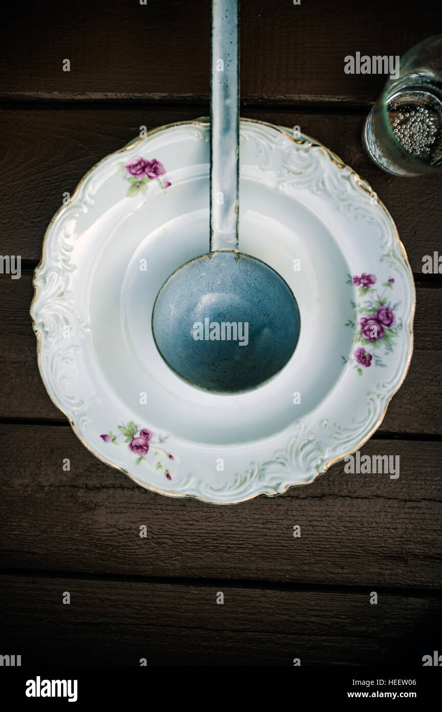 Smaltato mestolo nella piastra fiorito e bicchiere di acqua nella parte anteriore del tavolo in legno Foto Stock