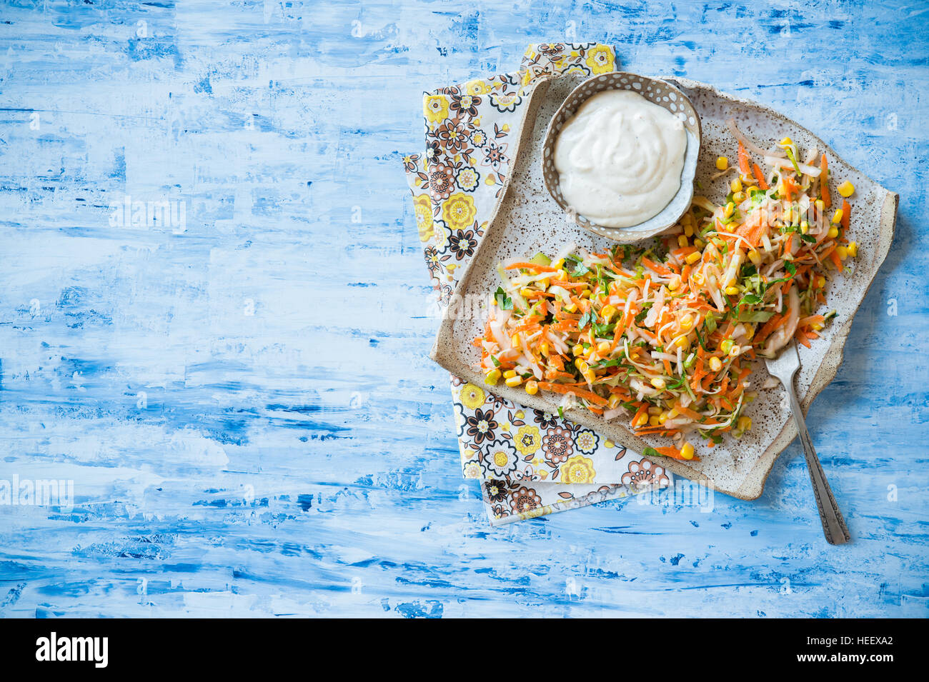 Cavoli freschi, il mais e la carota insalata coleslaw sulla piastra rustico, maionese medicazione sul lato. Sfondo blu, vista dall'alto, spazio di copia Foto Stock