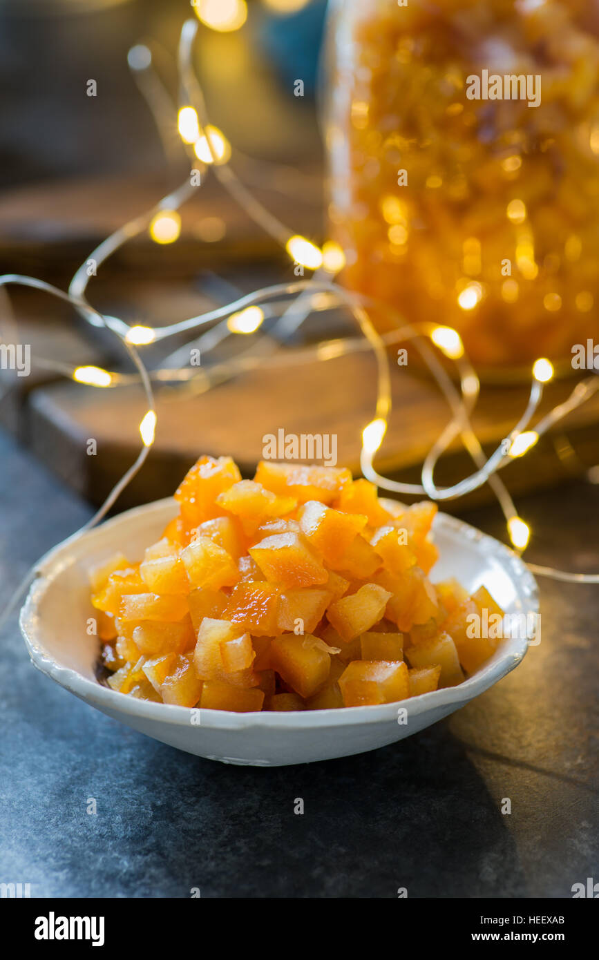 In casa di scorza d'arancia candita in ciotola su sfondo scuro, luci festive sul retro, il fuoco selettivo di Natale ingrediente di cottura Foto Stock