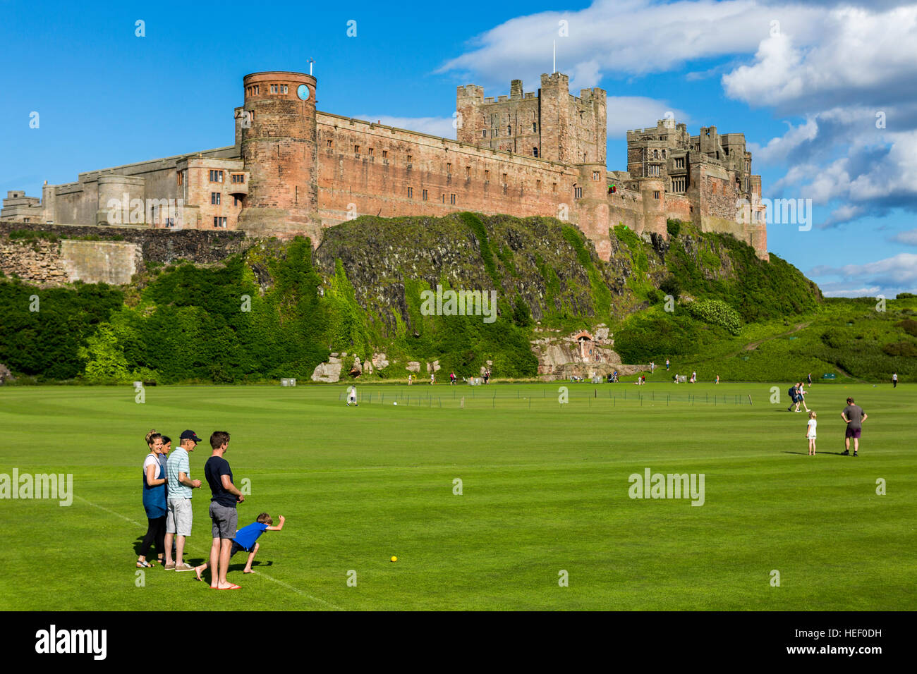 Un campo di gioco con i bambini a giocare a bocce ai piedi del castello di Bamburgh, Northumberland, Inghilterra, Regno Unito. Foto Stock