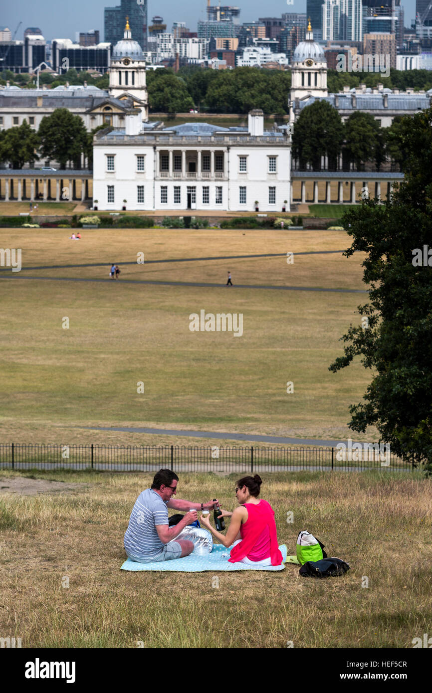 Una coppia avente un picnic nel parco di Greenwich con la Casa della Regina e la Old Royal naval College visibile, Londra, Regno Unito. Foto Stock