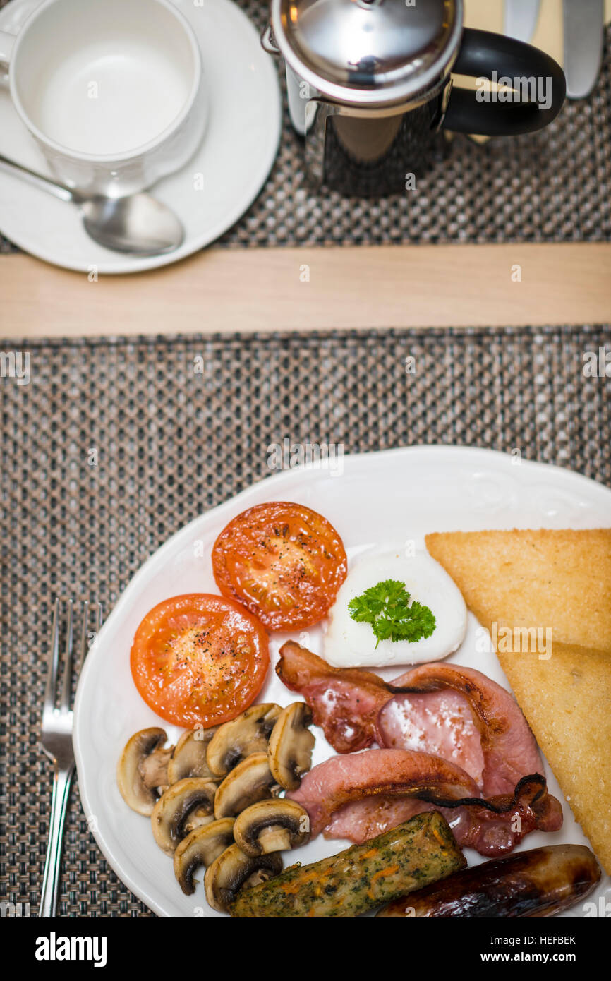 Full Monty: un fritto colazione inglese completa su una piastra bianca in un hotel del Regno Unito (pancetta, uova, salsicce, pomodori e funghi, pane fritto,) Foto Stock