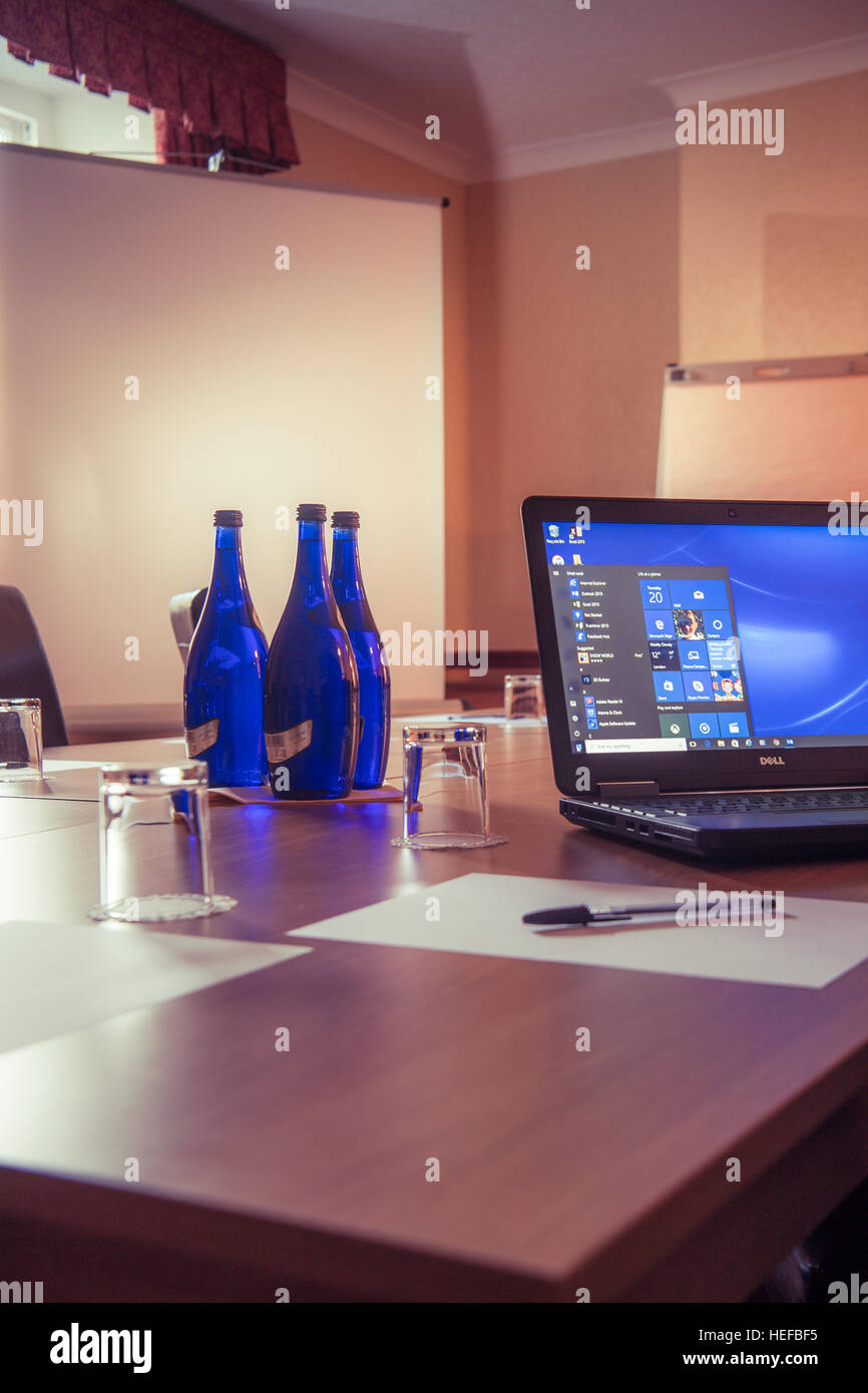 Un computer portatile e bottiglie di colore blu di Ty Nant acqua minerale sul tavolo durante una riunione di lavoro in una società boardroom REGNO UNITO Foto Stock