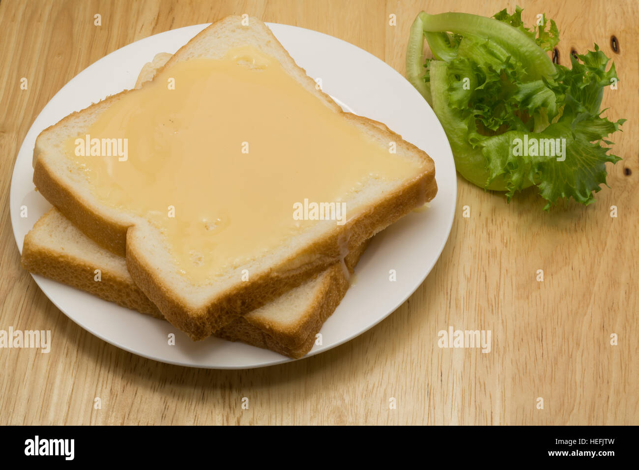 Pane e latte condensato zuccherato in una piastra bianca su una tavola di legno Foto Stock