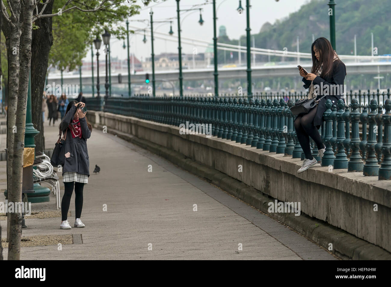 Budapest, Ungheria - Aprile 11,2016: una giovane ragazza cinese seduto sulla recinzione e giocare con il telefono cellulare. Foto Stock