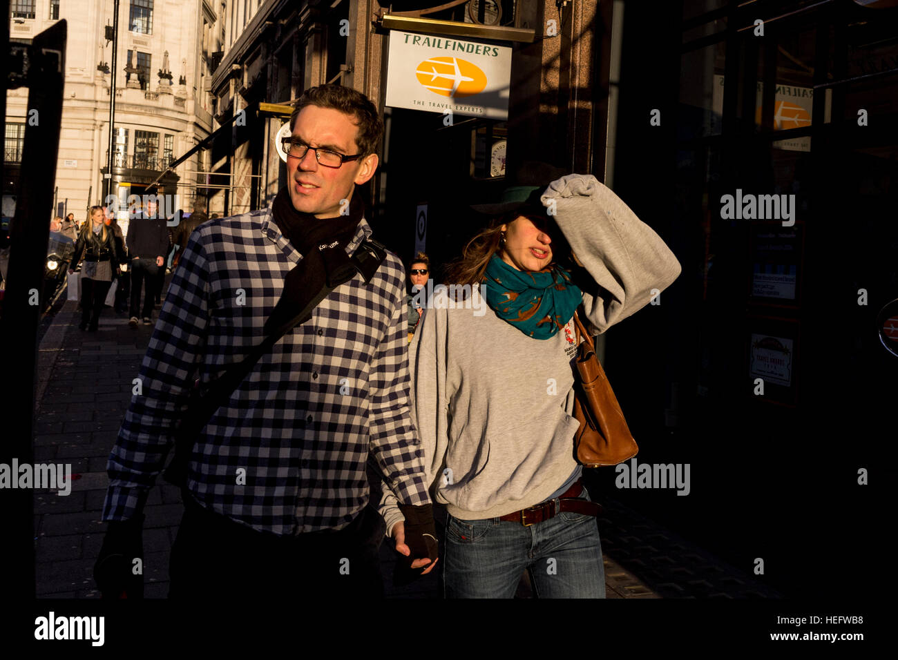 Una giovane coppia passeggiando lungo una strada di Londra al tramonto. La donna è schermare gli occhi dalla bassa sun Foto Stock