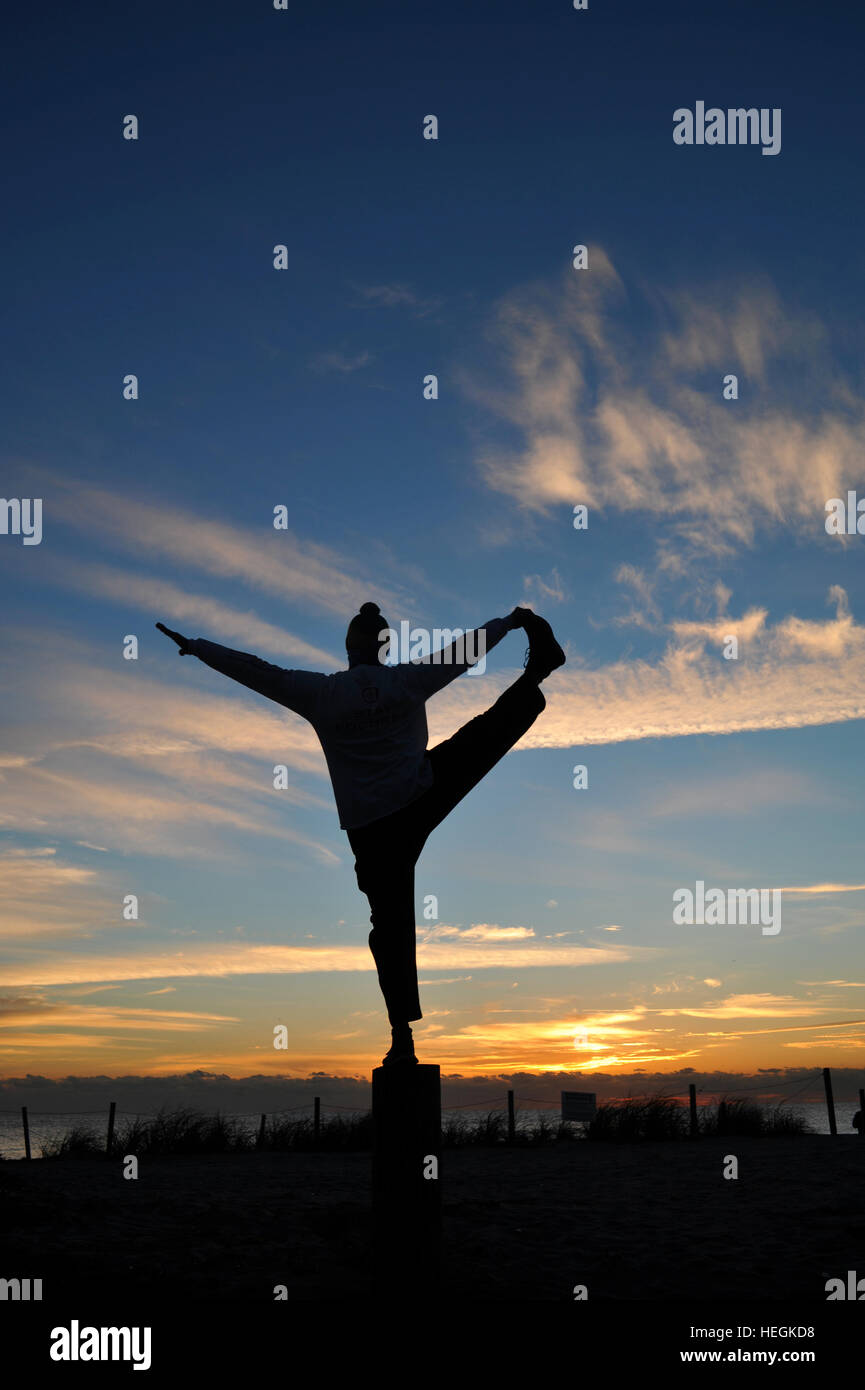 Stagliano l uomo nella posa di yoga in spiaggia durante il sorgere del sole. Foto Stock