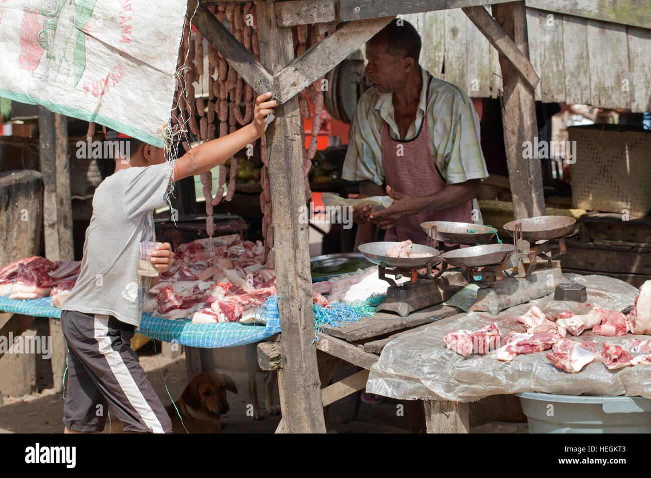 Ragazzo salsicce di acquisto da un macellaio in stallo. Strada del mercato. Sambava. A nord-est del Madagascar. Foto Stock