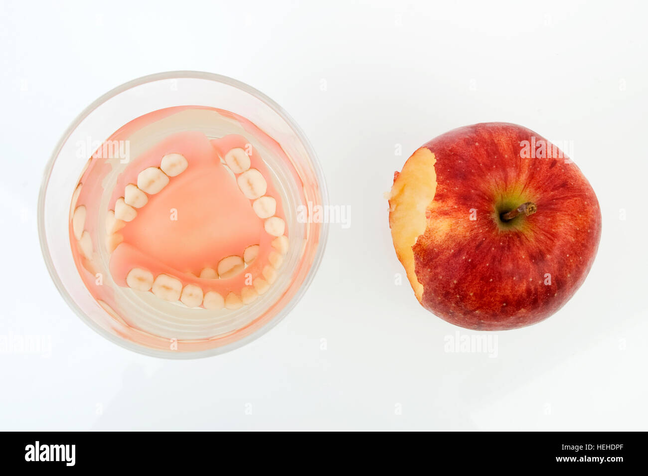 Falso denti, protesi in un bicchiere di acqua accanto a un Apple Foto Stock