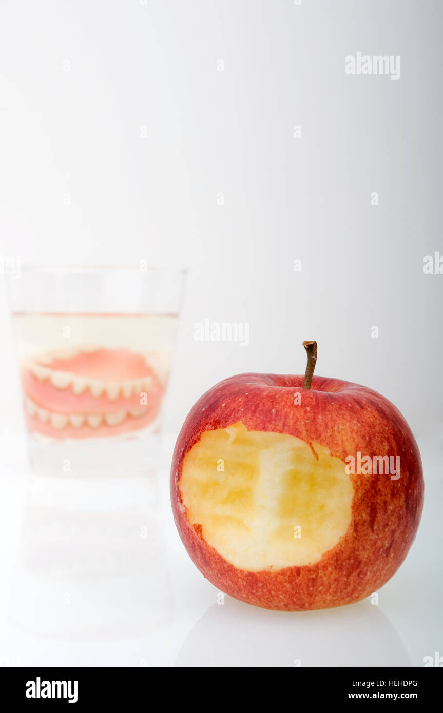 Falso denti, protesi in un bicchiere di acqua accanto a un Apple Foto Stock