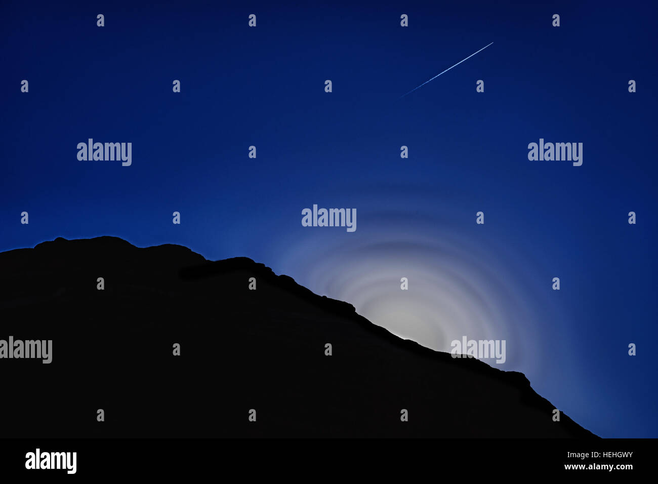 Un drammatico evento solare.L'impostazione sun una contrail ed il silo di una roccia su un cielo blu scuro. Foto Stock