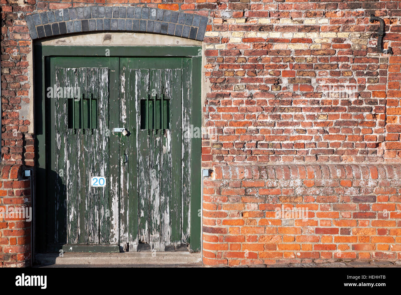 Vecchio dock bloccato le porte laterali seduti in un mal riparato parete. Doppie porte con finestra di barre per la sicurezza e la pelatura della vernice verde. Foto Stock