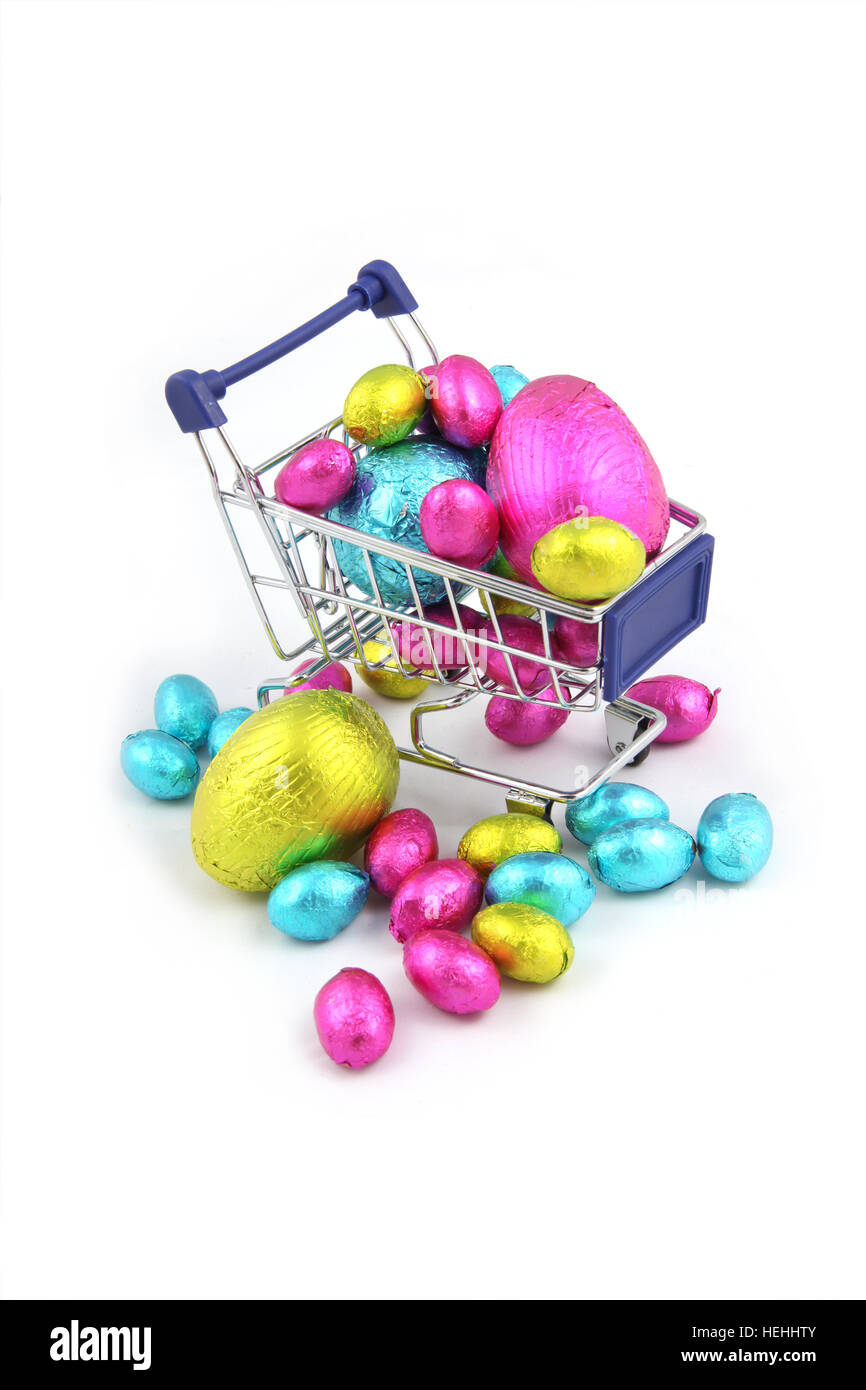 Colorate le uova di Pasqua di cioccolata in involucro di carta metallizzata, e seduto in un carrello della spesa da un super mercato su uno sfondo bianco. Foto Stock