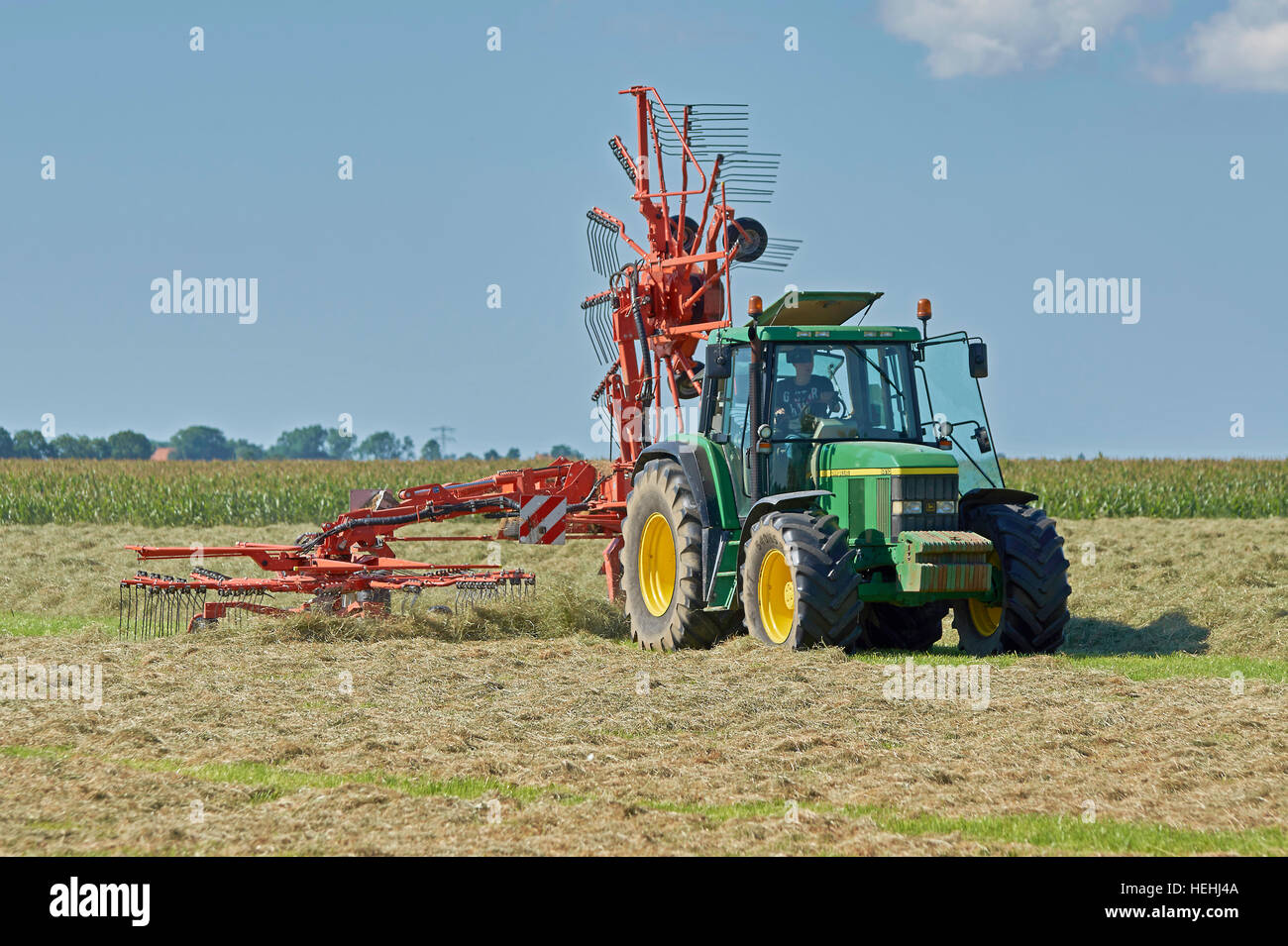 Un John Deere trattore 6610 con un Kuhn rastrello rotante usando un rotore per realizzare andane piccole per la rapida asciugatura del fieno. Foto Stock