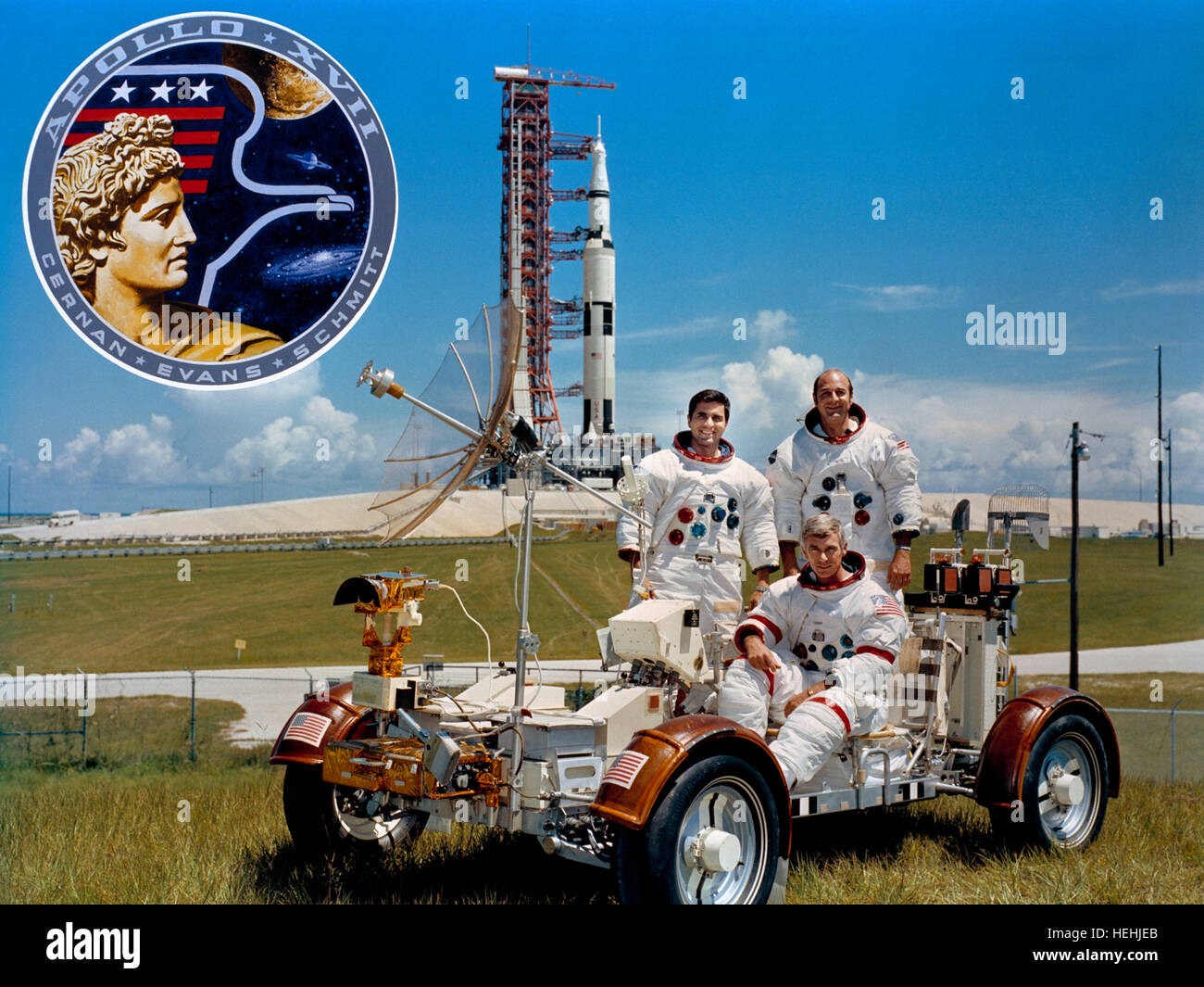 La NASA Apollo 17 atterraggio lunare missione il primo equipaggio astronauti (L-R) Harrison Schmitt, Gene Cernan e Ronald Evans pratica agendo lunare veicolo itinerante trainer con l'Apollo 17 Saturn V veicolo spaziale in background al Kennedy Space Center il 30 settembre 1971 nei pressi di Merritt Island, Florida. Foto Stock