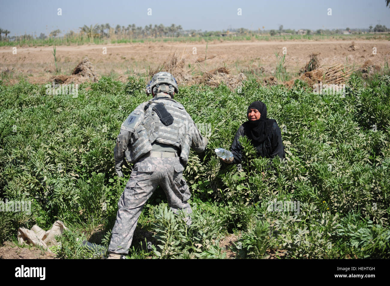 Stati Uniti Army Sgt. 1. Classe Shane Perret (sinistra) da Salina, Kan., assegnato alla Società Delta, 1° Battaglione Armor, 63reggimento blindato, 2° Brigata Team di combattimento, 1° Divisione di Fanteria, dà un acqua in bottiglia per un iracheno le donne a lavorare in una fattoria in Mahmudiyah, Iraq il 27 marzo, durante una pattuglia attraverso il villaggio. Pattuglia in Mahmudiyah, Iraq 161381 Foto Stock
