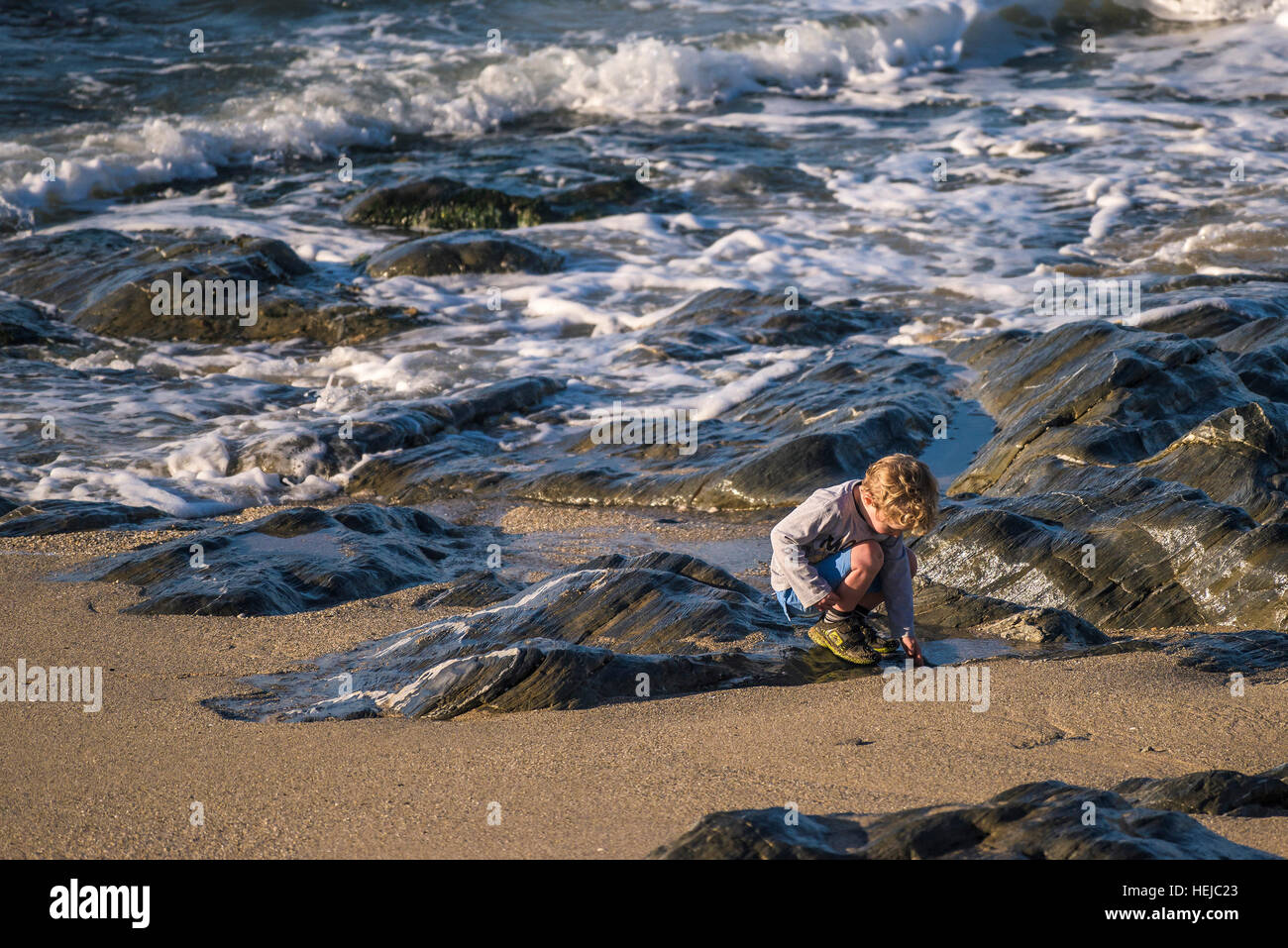 Un giovane ragazzo esplora la riva del mare a poco Fistral in Newquay, Cornwall Foto Stock