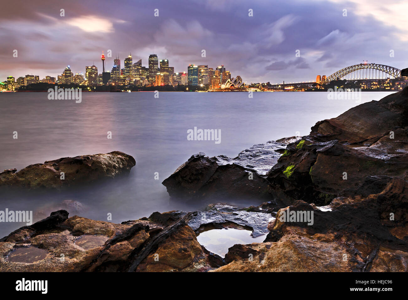 Sydney Harbour sabbia rocce di pietra a bassa marea contrastante CBD della città i punti di riferimento dal Ponte del Porto di grattacieli e torri. Foto Stock