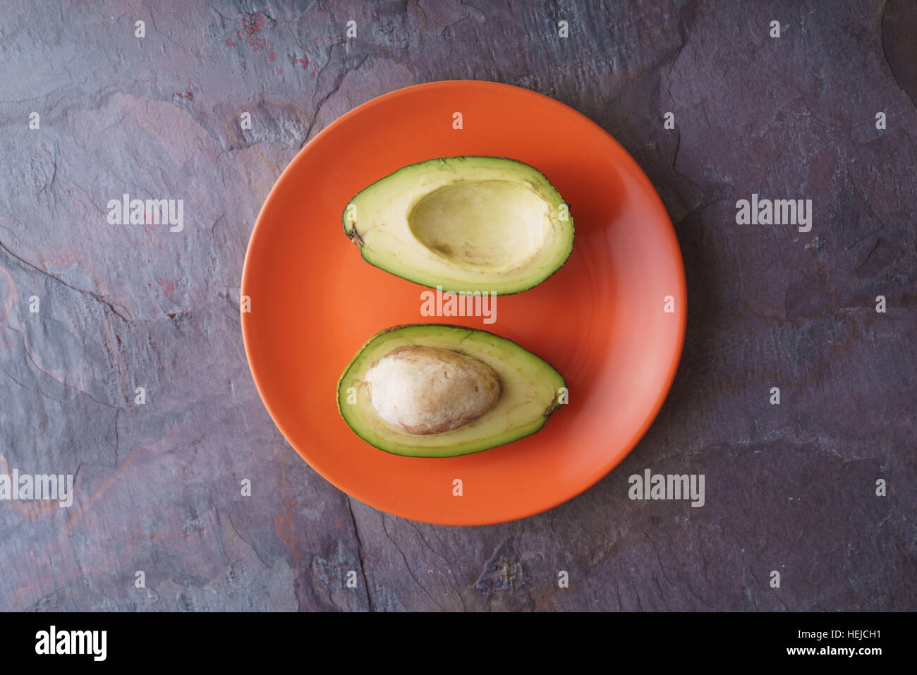 Metà di Avocado giacciono su una piastra di colore arancione su una orizzontale di ardesia Foto Stock