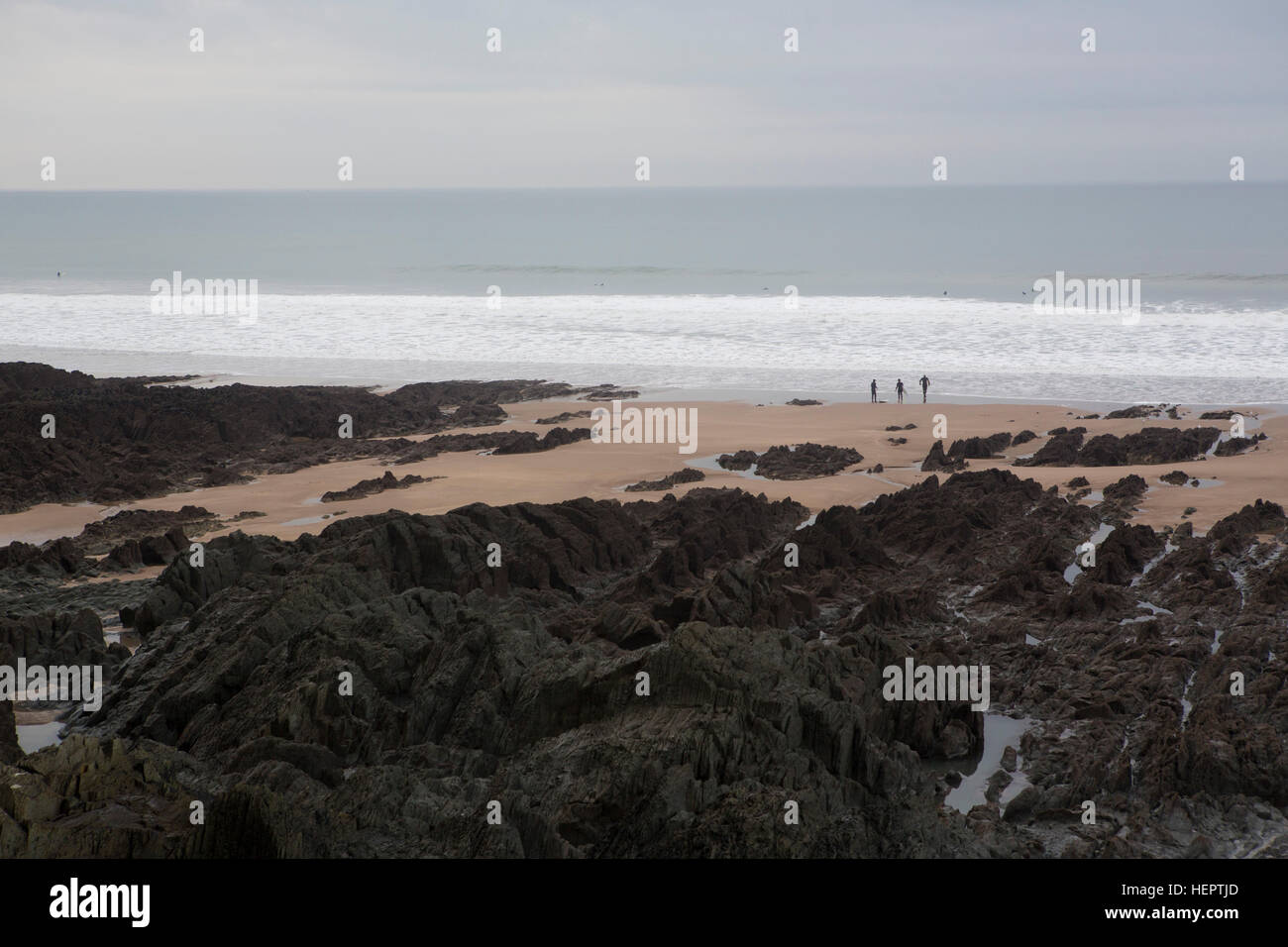 Surfers stand sul bordo del mare in attesa di entrare in acqua su una spiaggia nel Regno Unito. Foto Stock