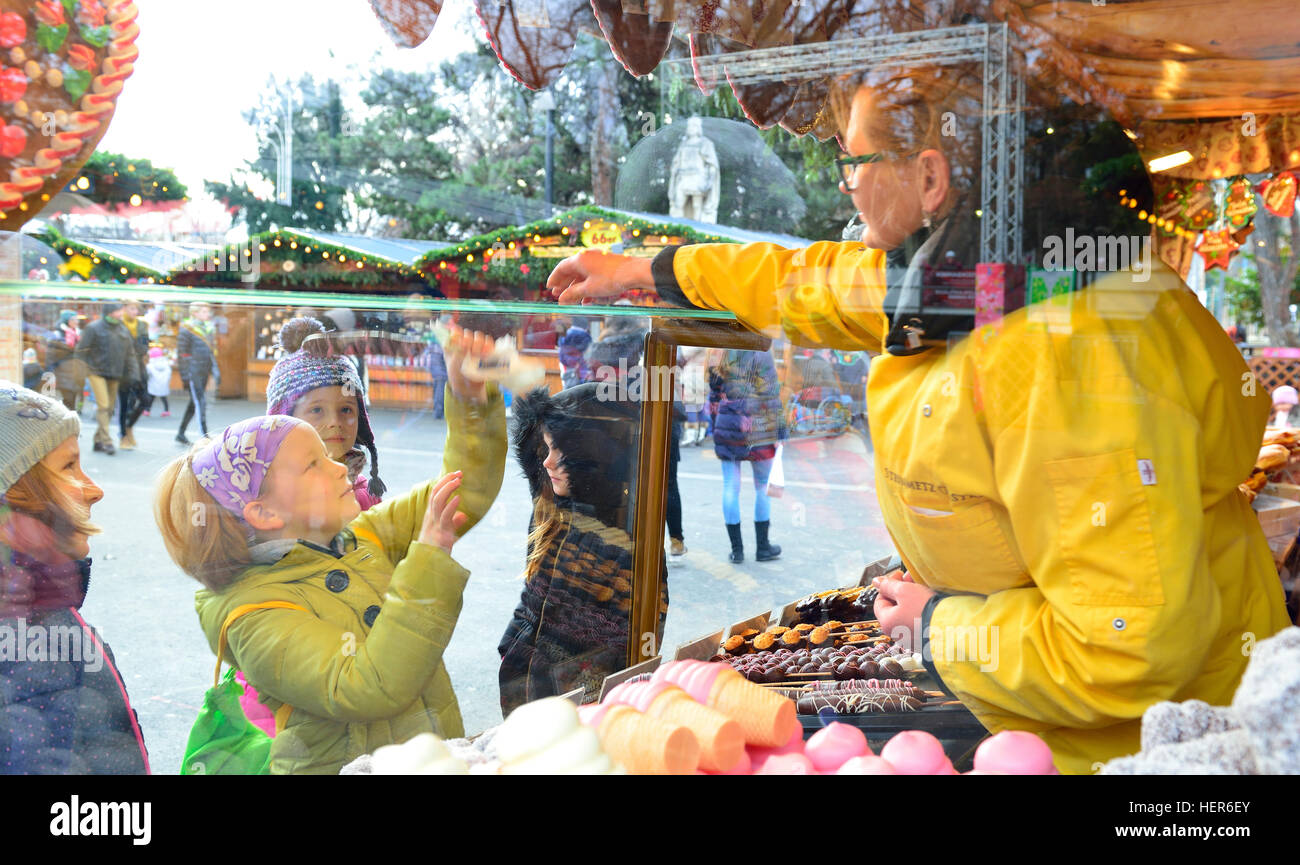I bambini in una bancarella dolce e torta pagano per loro Acquisti a Rathauspark (Rathausplatz) Mercatino di Natale, Vienna, Austria Foto Stock