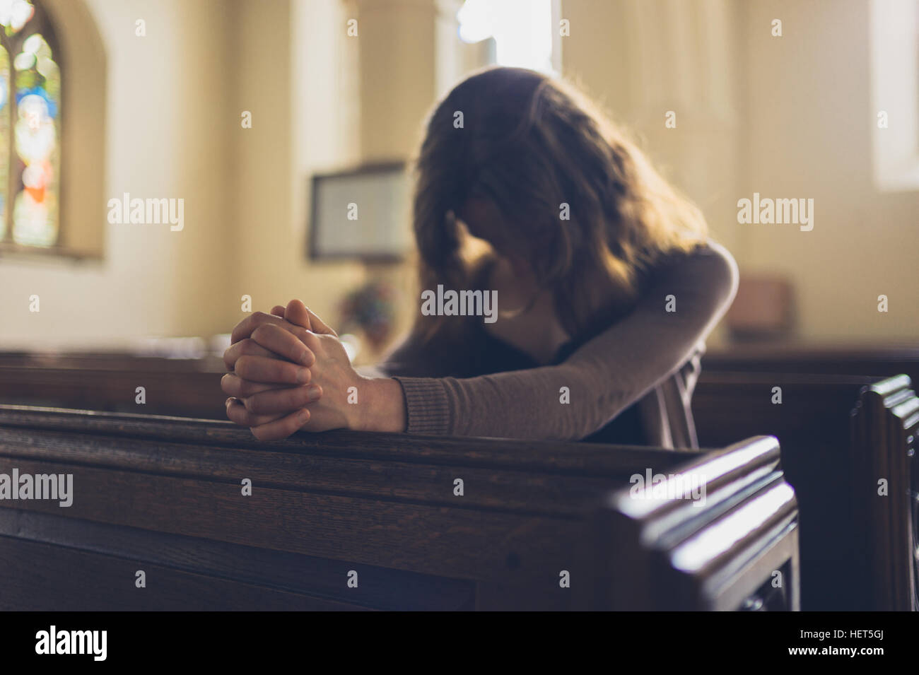 Una giovane donna è seduta con le mani giunte e sta pregando in una chiesa Foto Stock