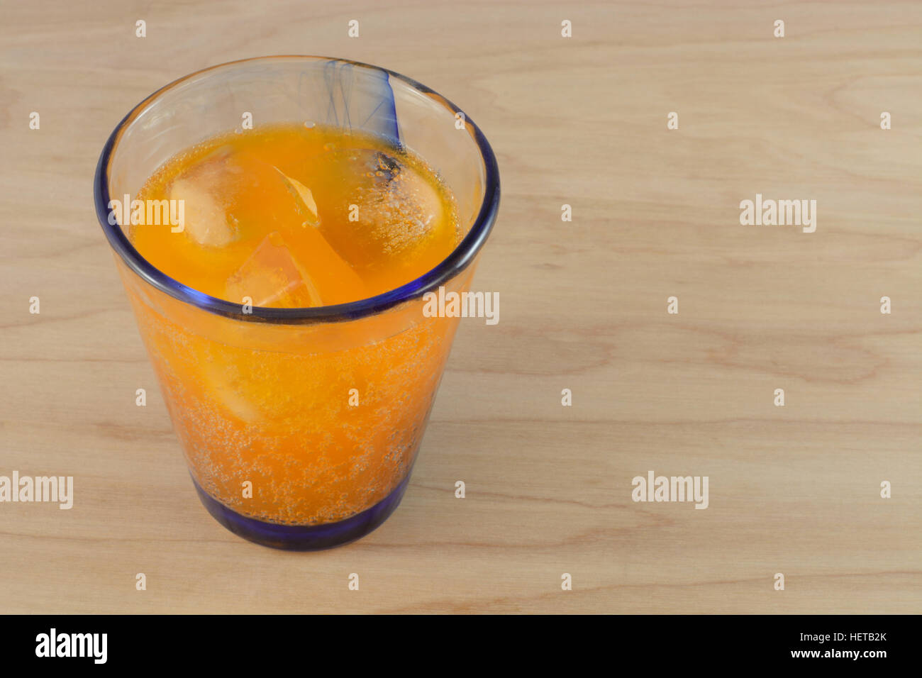Soda arancione pop con cubetti di ghiaccio nel bicchiere sul tavolo di legno Foto Stock
