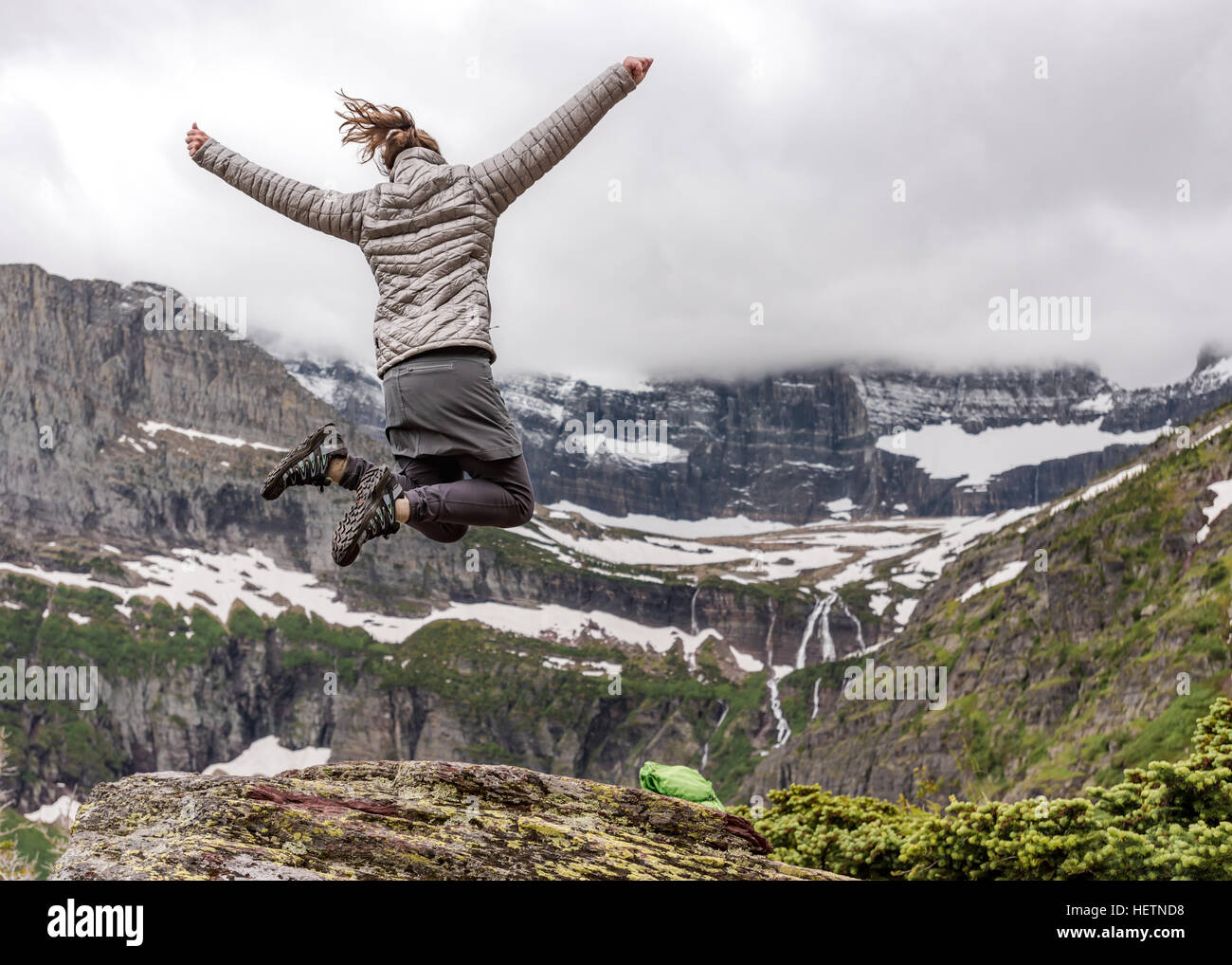 Donna in abiti caldi salta in eccitazione che si affaccia sulle montagne del Montana Foto Stock