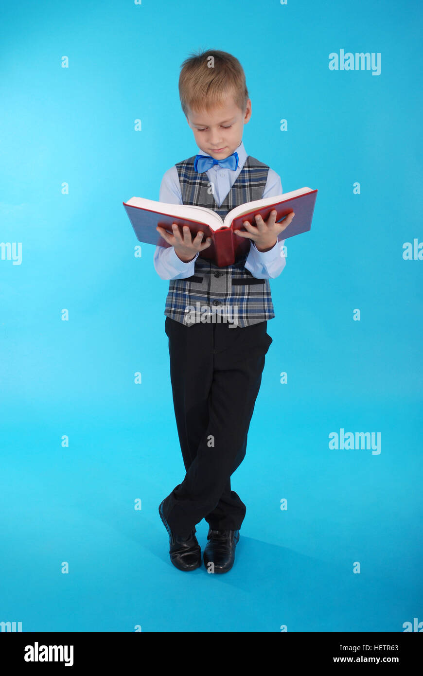 Ragazzo in uniforme scolastica lettura libro aperto su uno sfondo blu Foto Stock