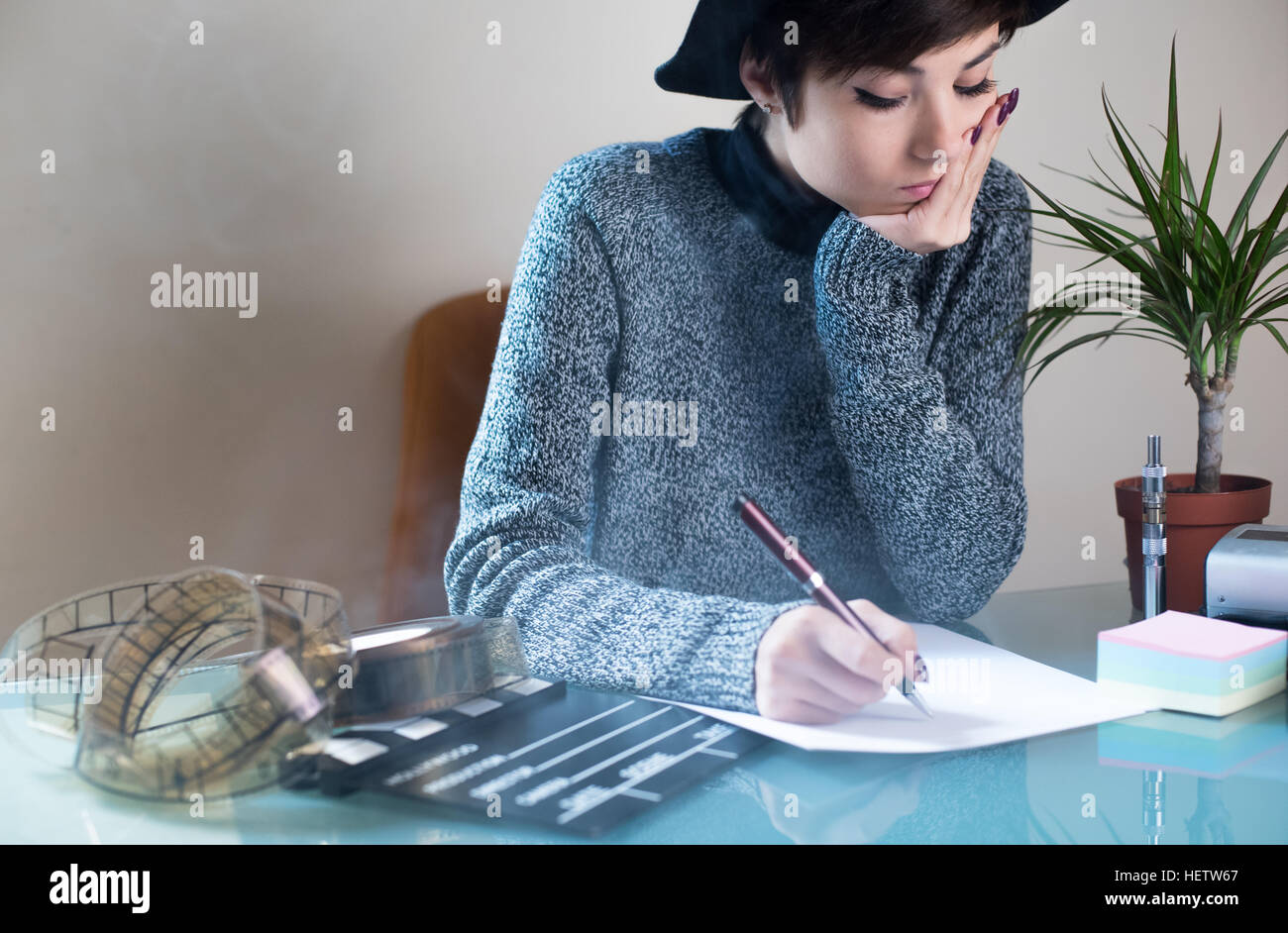 Giovane donna graziosa la scrittura su desktop con oggetti filmato, clapper e filmina con il fumo di sigaretta in aria Foto Stock