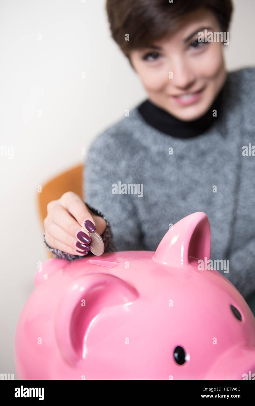 Giovane donna sorridente sfocati sullo sfondo mettendo coin in rosa piggy box Foto Stock