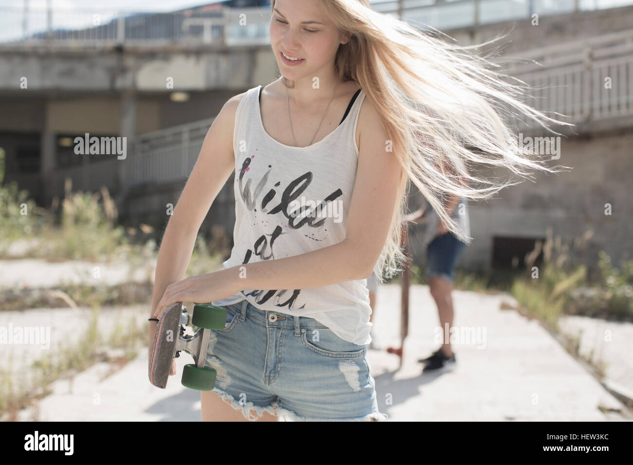 Guidatore di skateboard nel serbatoio superiore con selvaggio a cuore lo slogan, amici in background Foto Stock