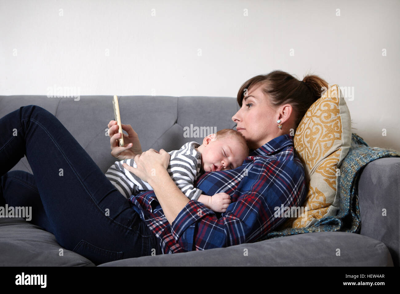 Madre con bambino sdraiato sul divano guardando smartphone Foto Stock